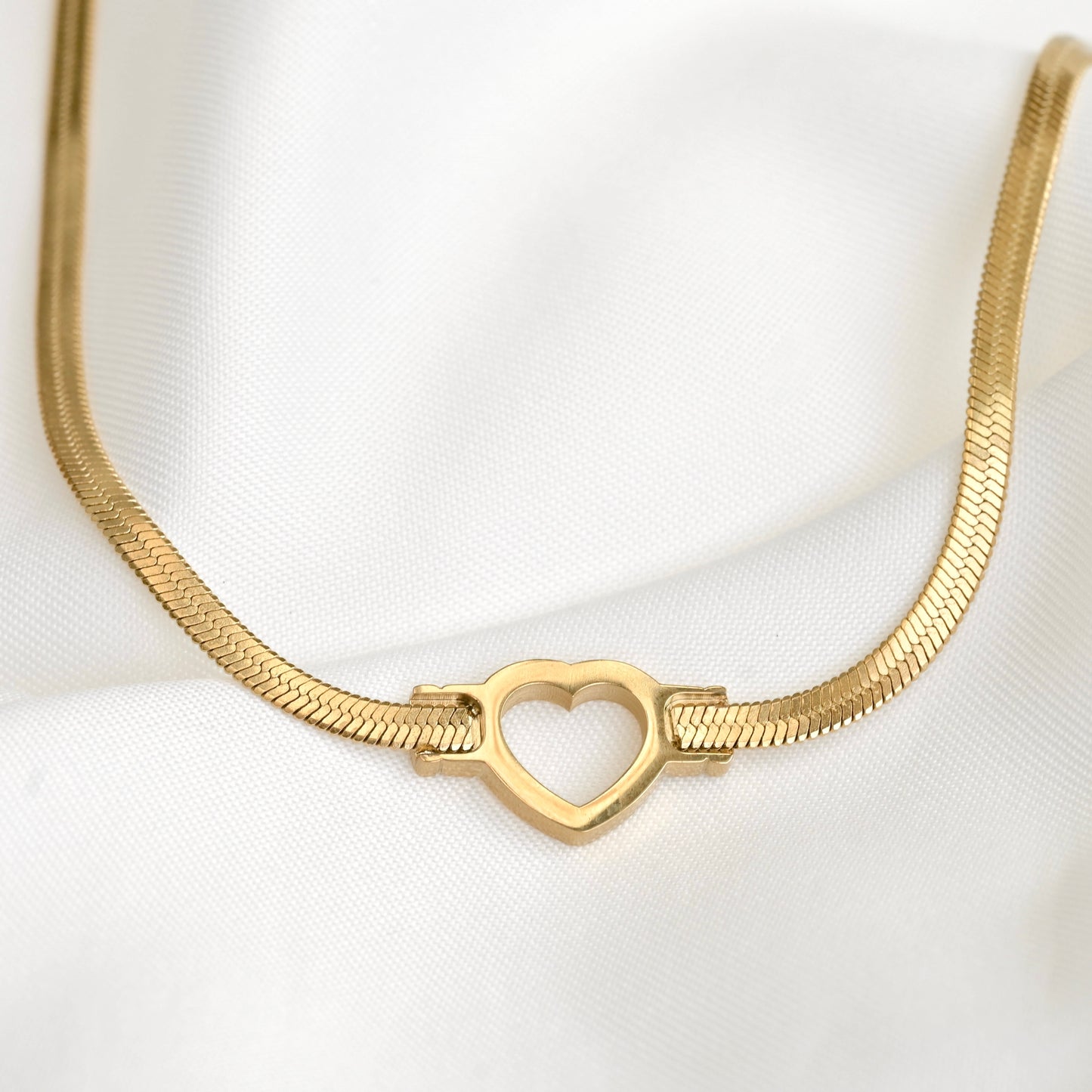Gold heerigbone necklace with a heart-shaped charm on a white background