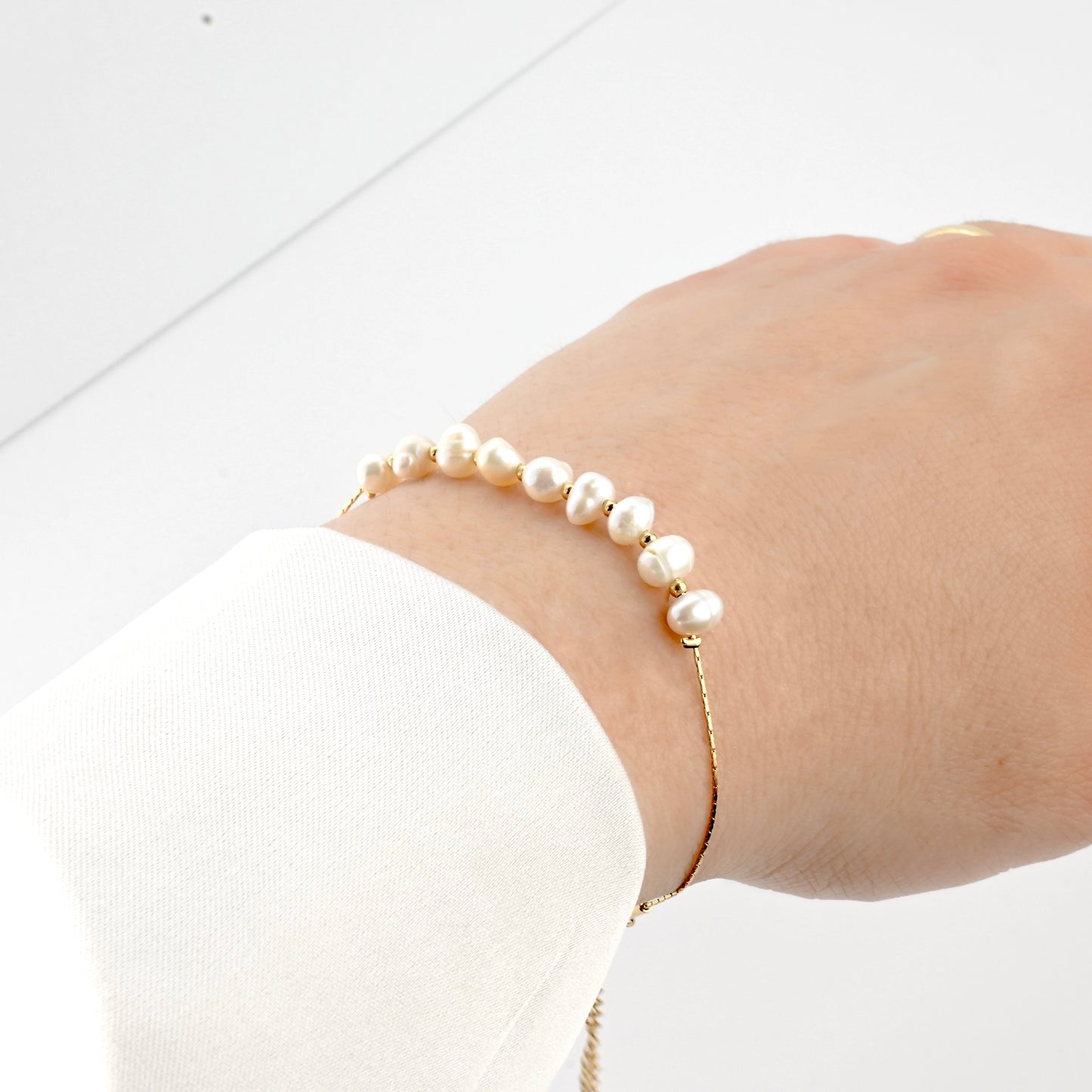Gold pearl bracelet with gold spacer beads and a delciate shimmering chainon a person's wrist with a white background