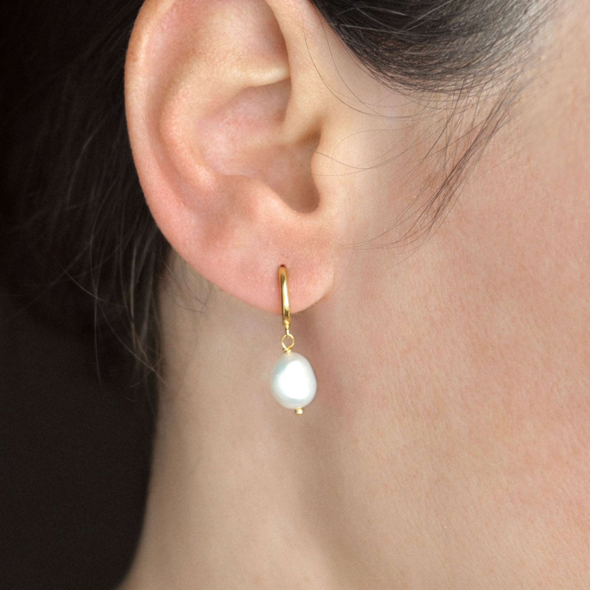 gold plated sterling silver pearl earring on a person's ear with a dark background