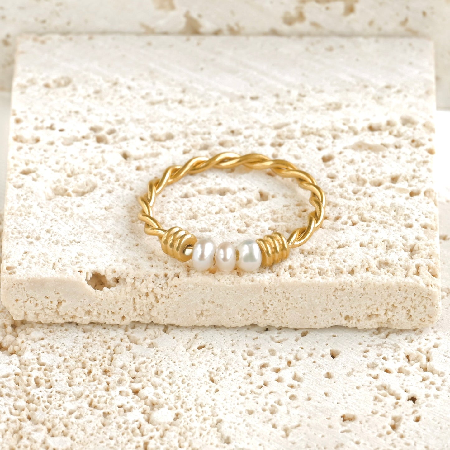 Gold twisted band with 3 tiny pearl centerpiece on a textured beige surface