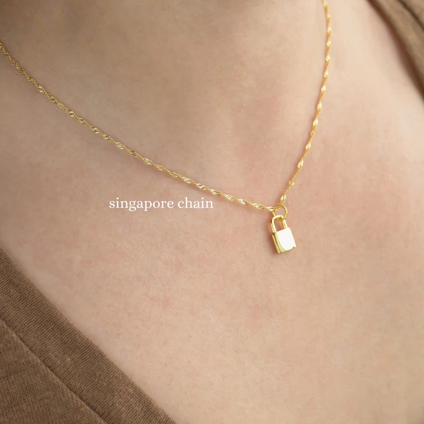Gold twisted chain necklace with a lock pendant on a person wearing a brown top.