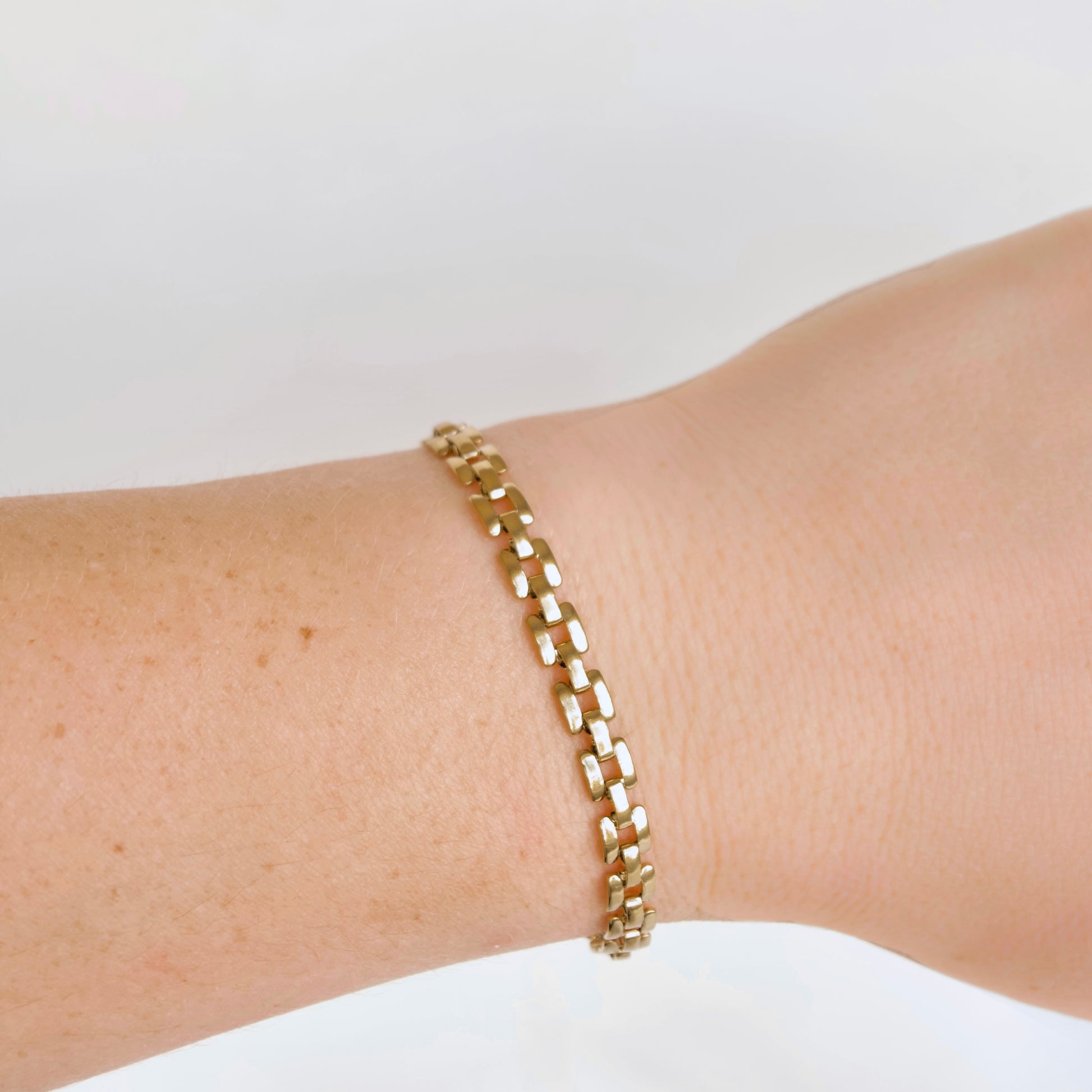A gold-toned metal link bracelet with a polished, geometric, interlocking design, shown worn on a person's wrist against a plain white background.