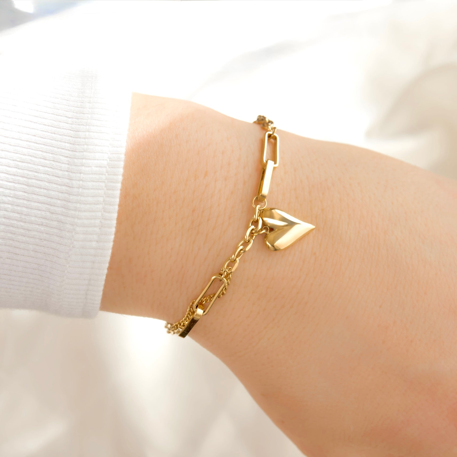 A delicate gold mixed chain bracelet with a geometric link design and a small arrow charm, shown worn on a person's wrist.