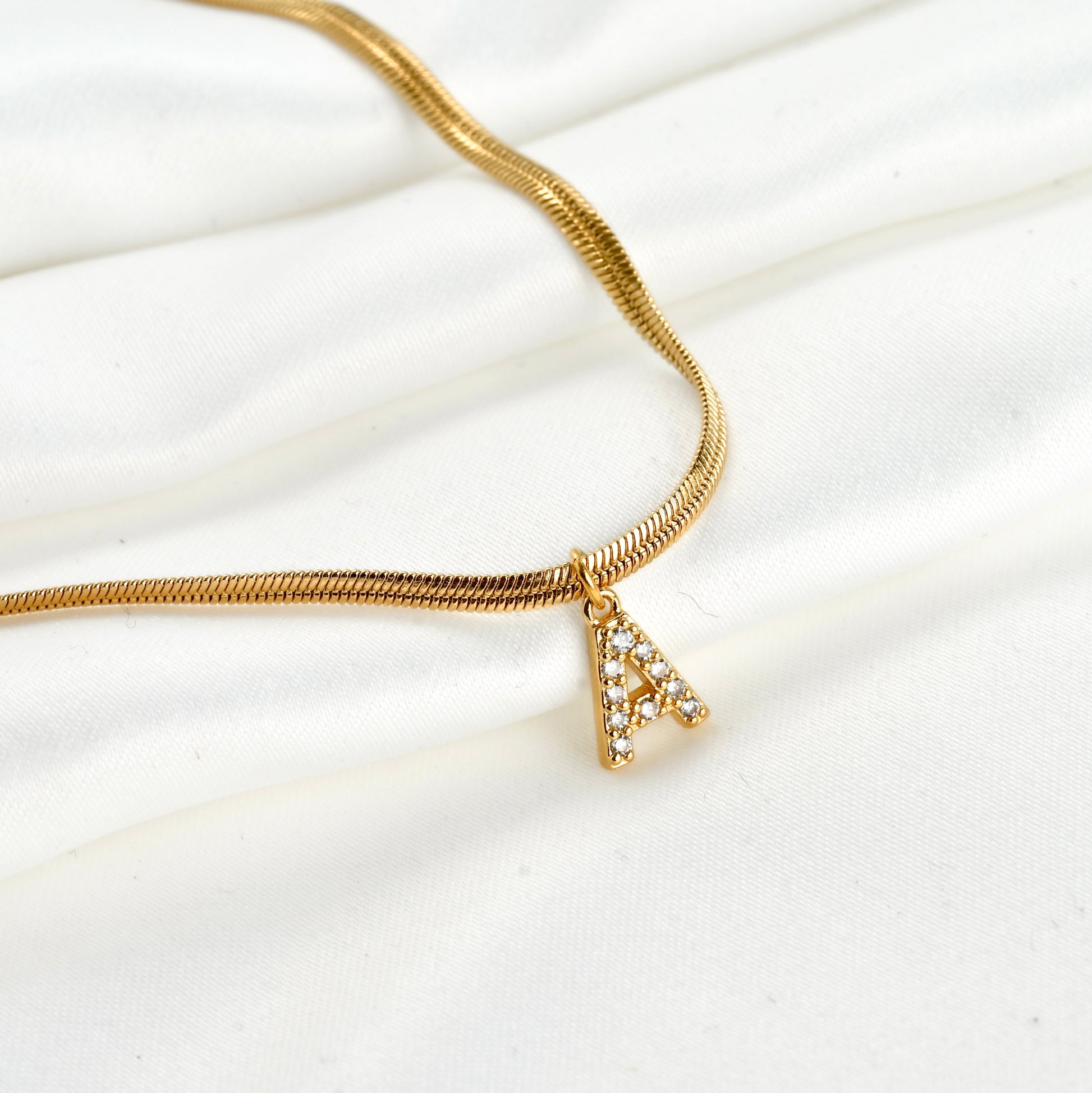 Gold necklace with an initial pendant 'A' with embedded stones on a white fabric background