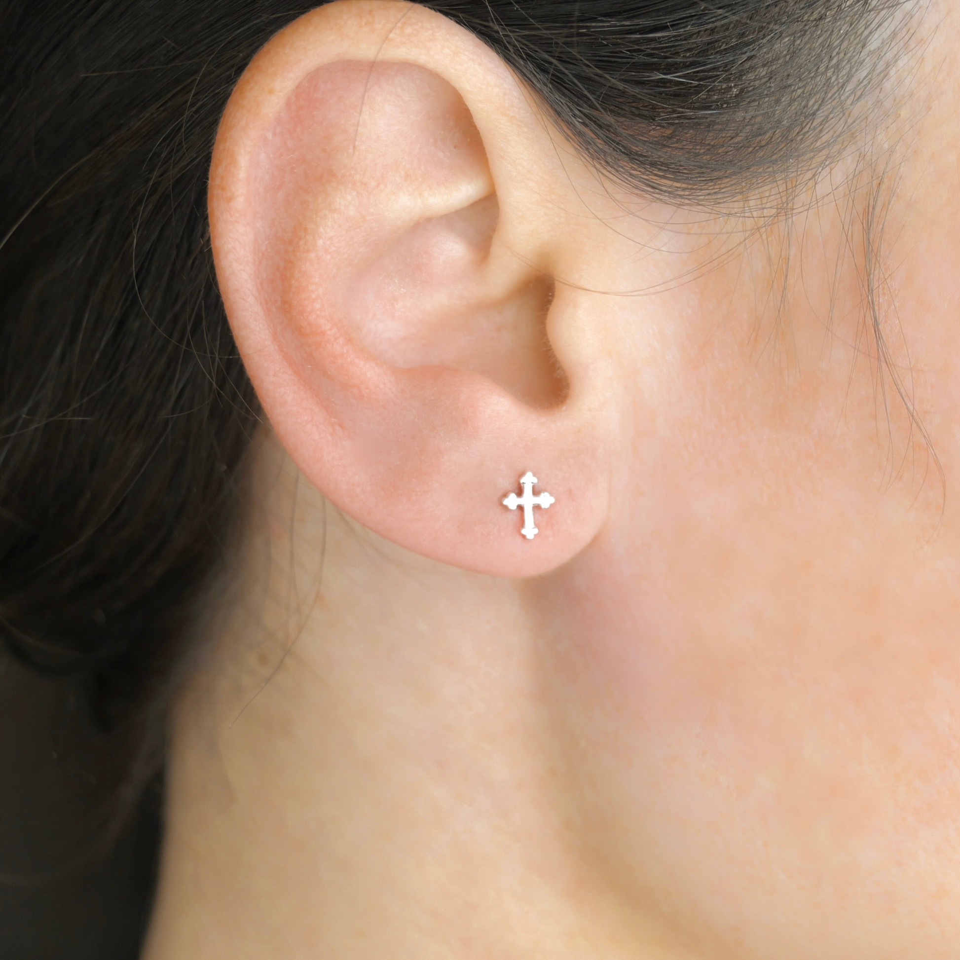 Close-up of an ear wearing a small silver cross earring.