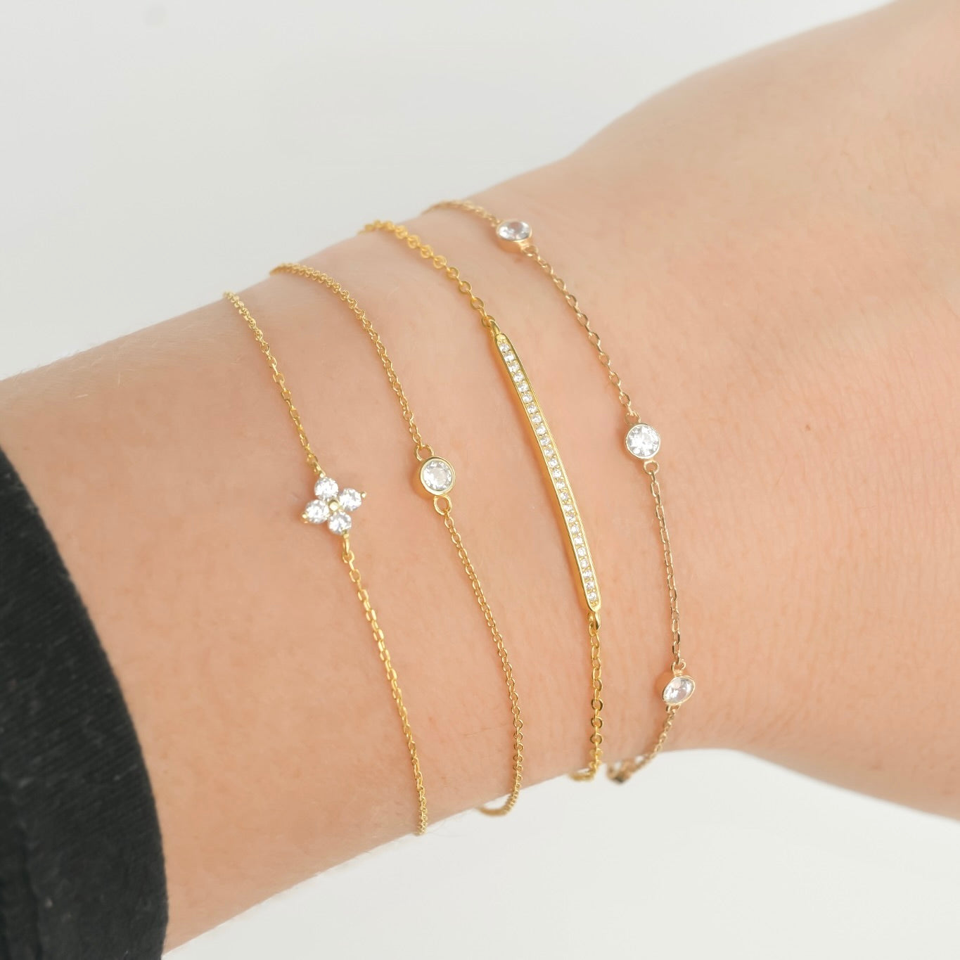 Gold CZ bracelets with small clear stones layered on a wrist against a neutral background