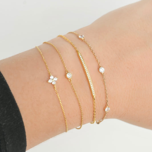 Gold CZ bracelets with small clear stones layered on a wrist against a neutral background