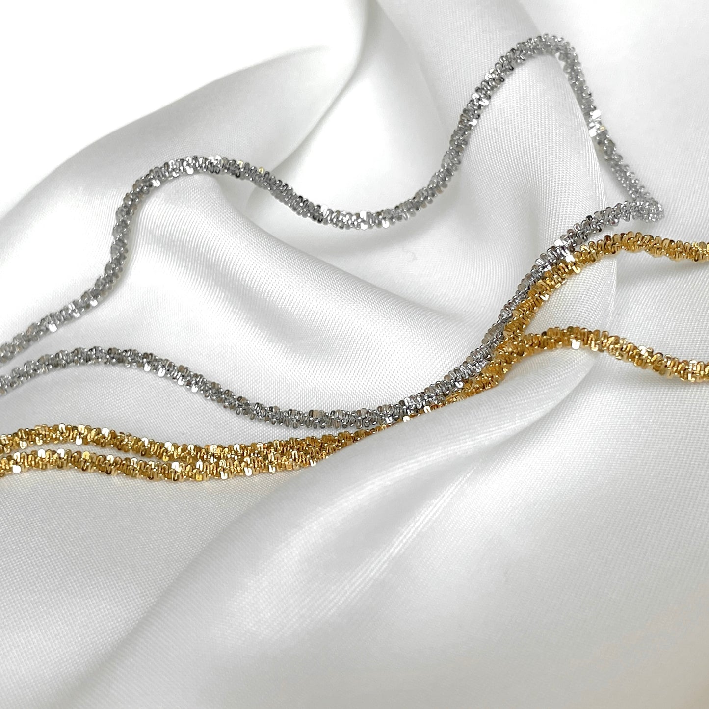 Two gold and silver chains on a white fabric background