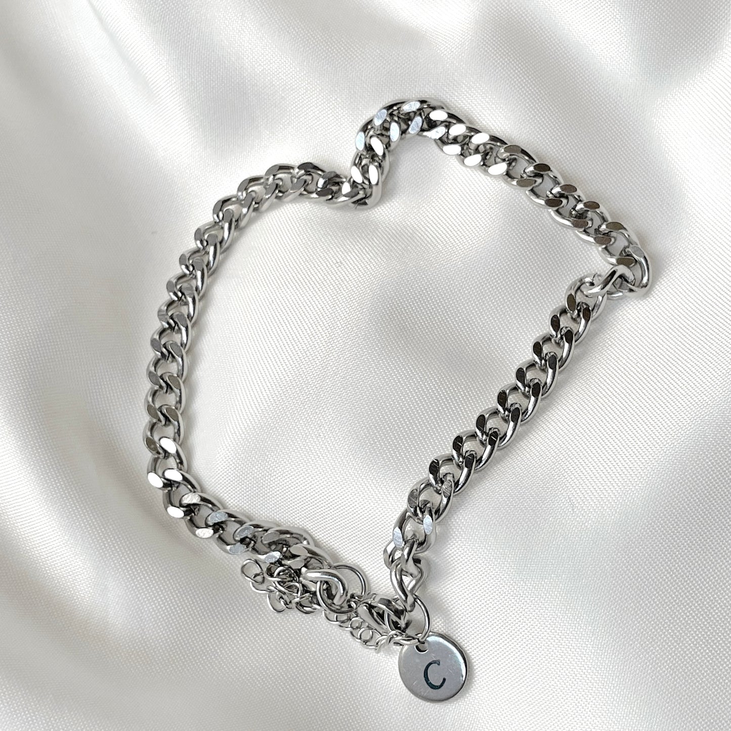 Silver chain bracelet with a round initial  charm on a white satin background