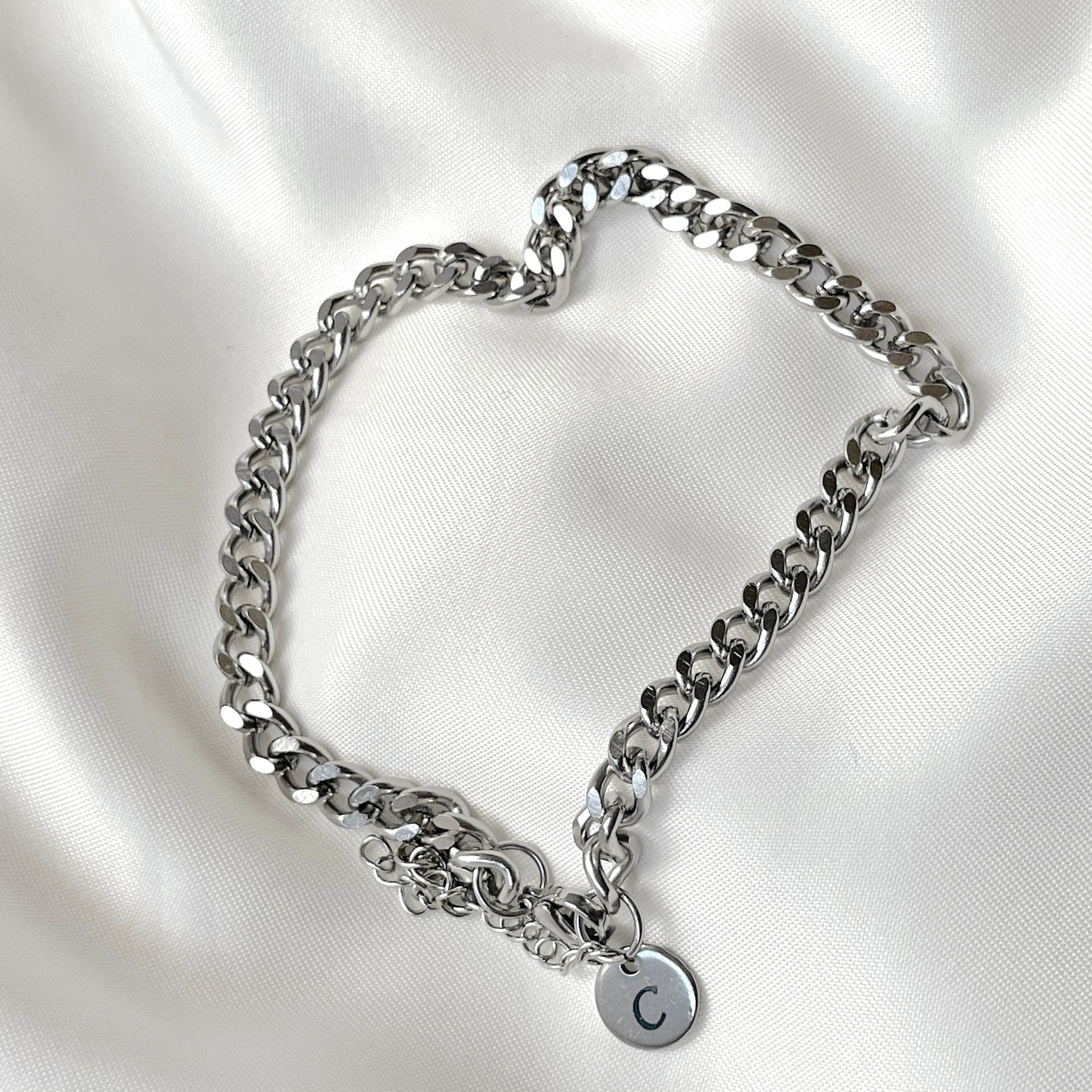 Silver chain bracelet with a round initial  charm on a white satin background