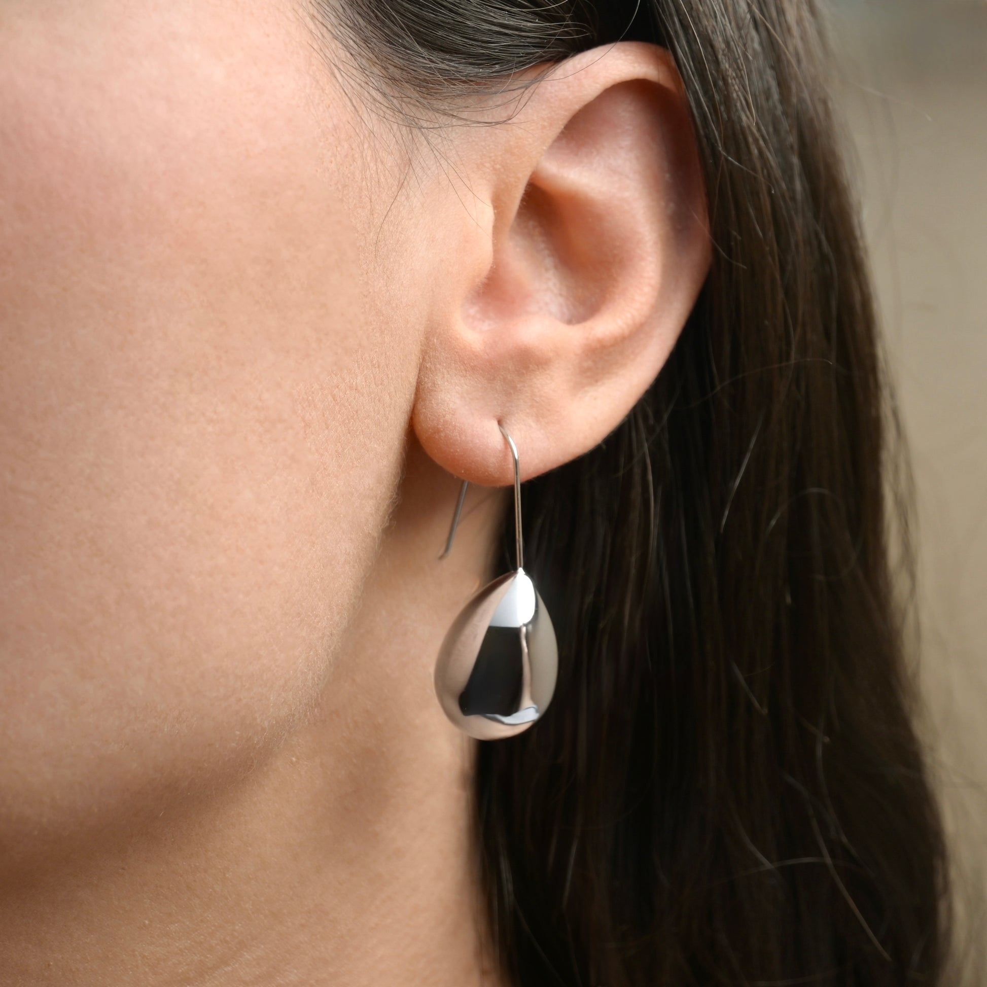 Close-up of an ear wearing a large teardrop-shaped earring with a blurred background