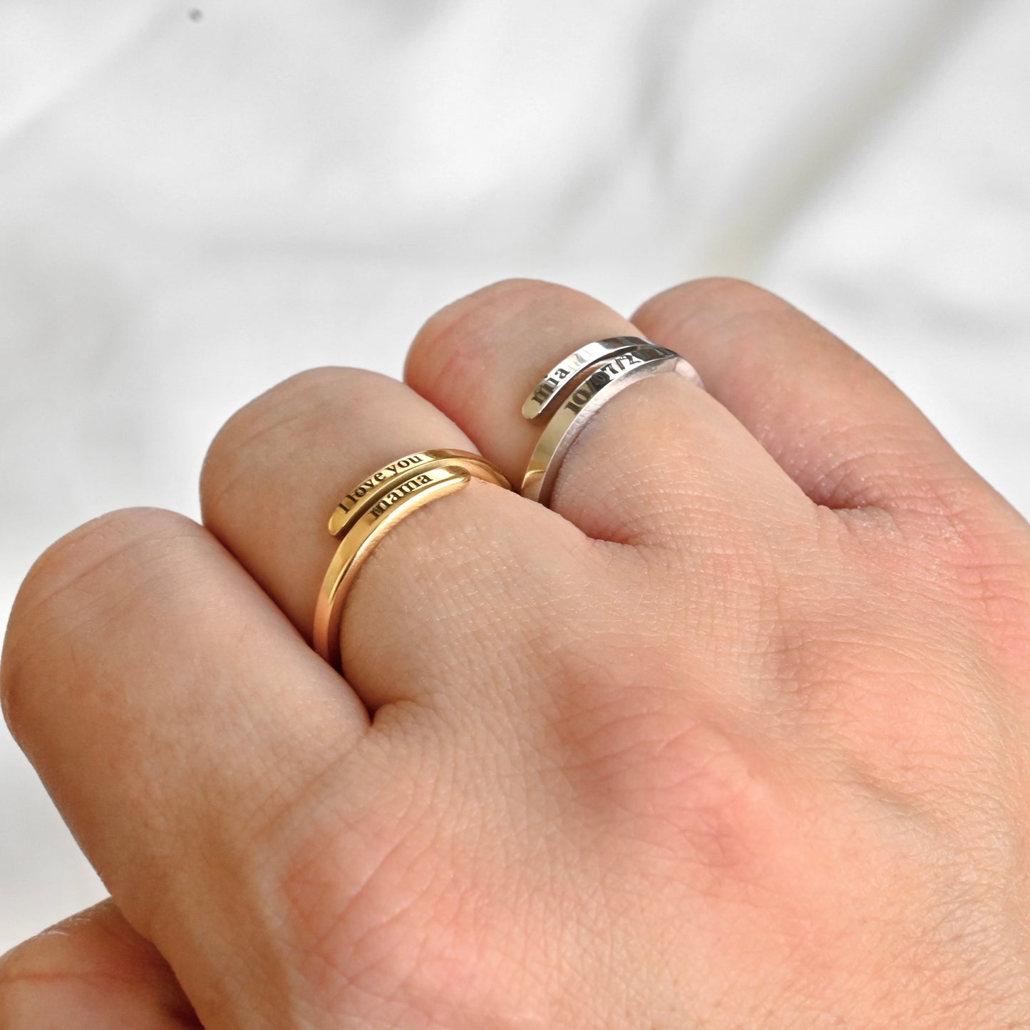 Two dainty gold engraved rings, one gold and one silver,  on a person's finger against a white background