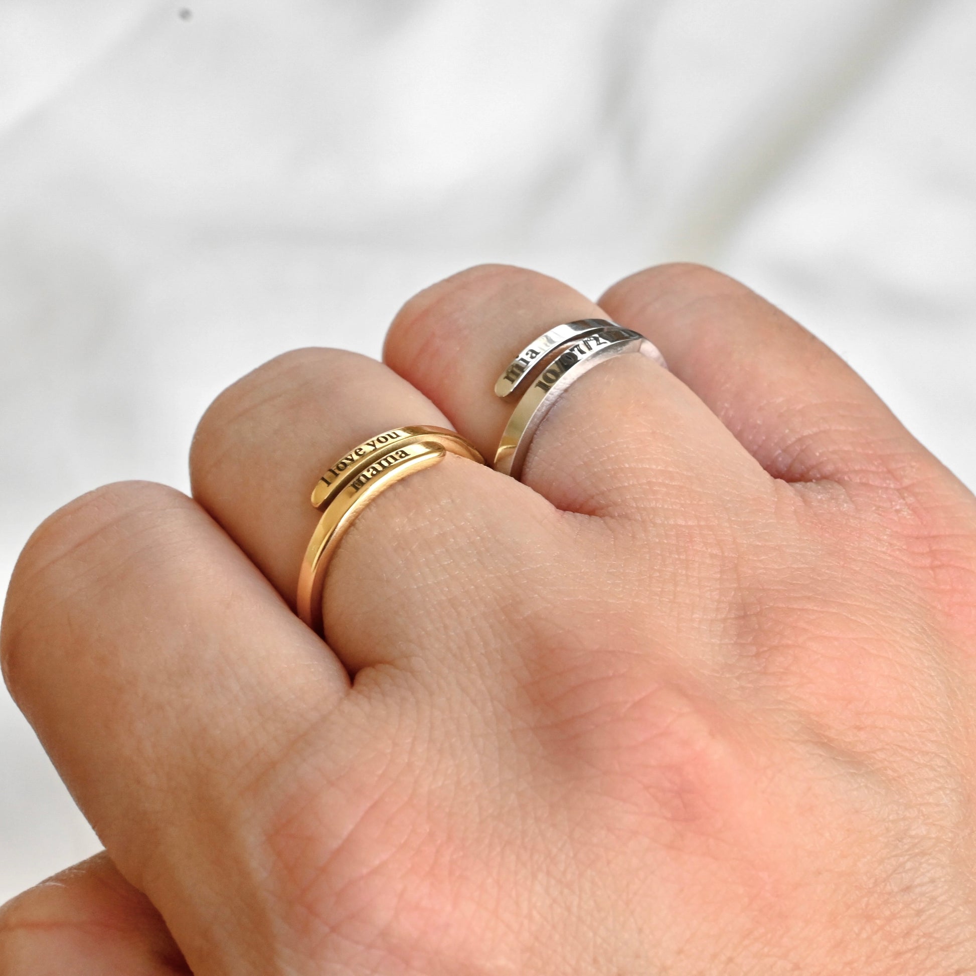 Two dainty gold engraved rings, one gold and one silver,  on a person's finger against a white background