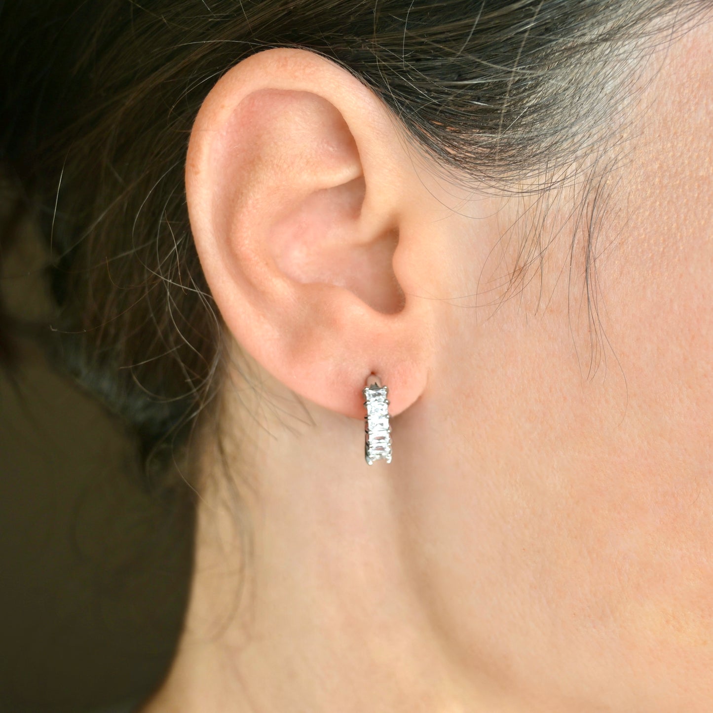 Close-up of an ear wearing a silver baguette hoop earring with a blurred background