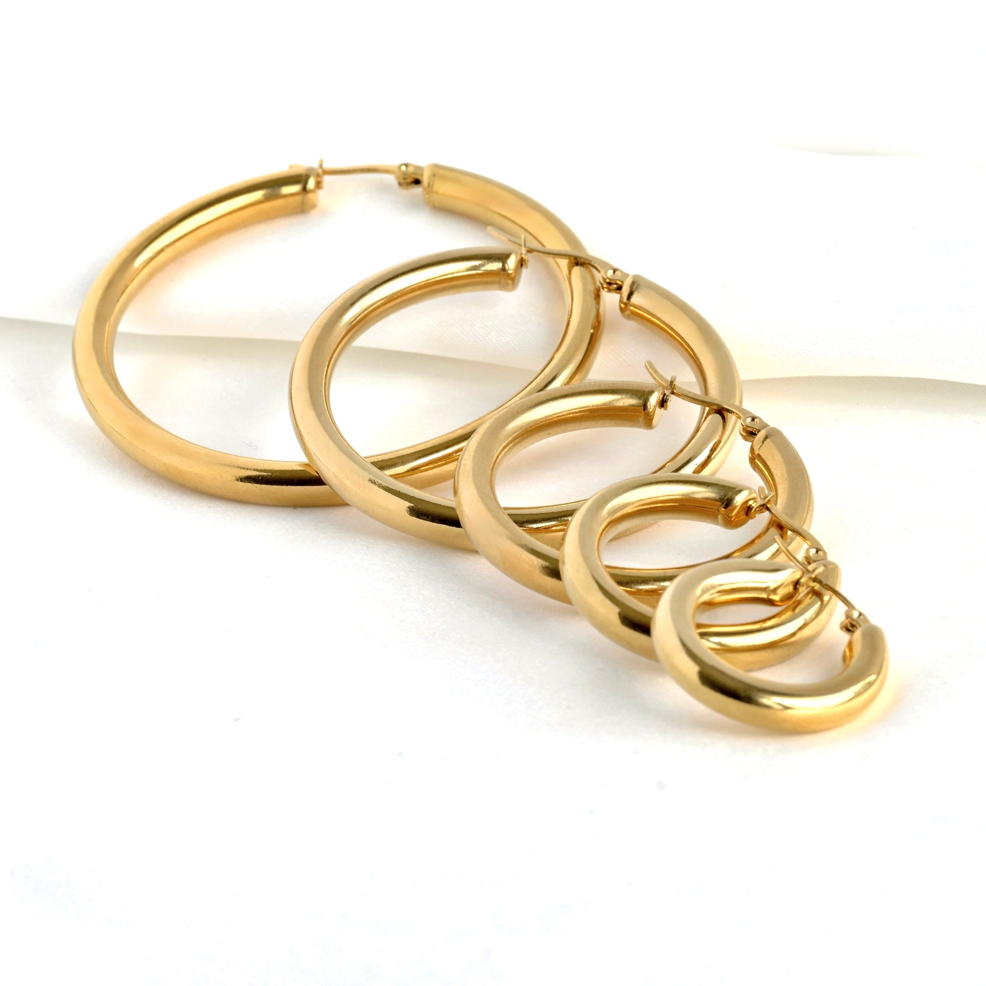 Set of chunky gold hoop earrings in 5 different sizes stacked from 25mm to 60mm, on a white background