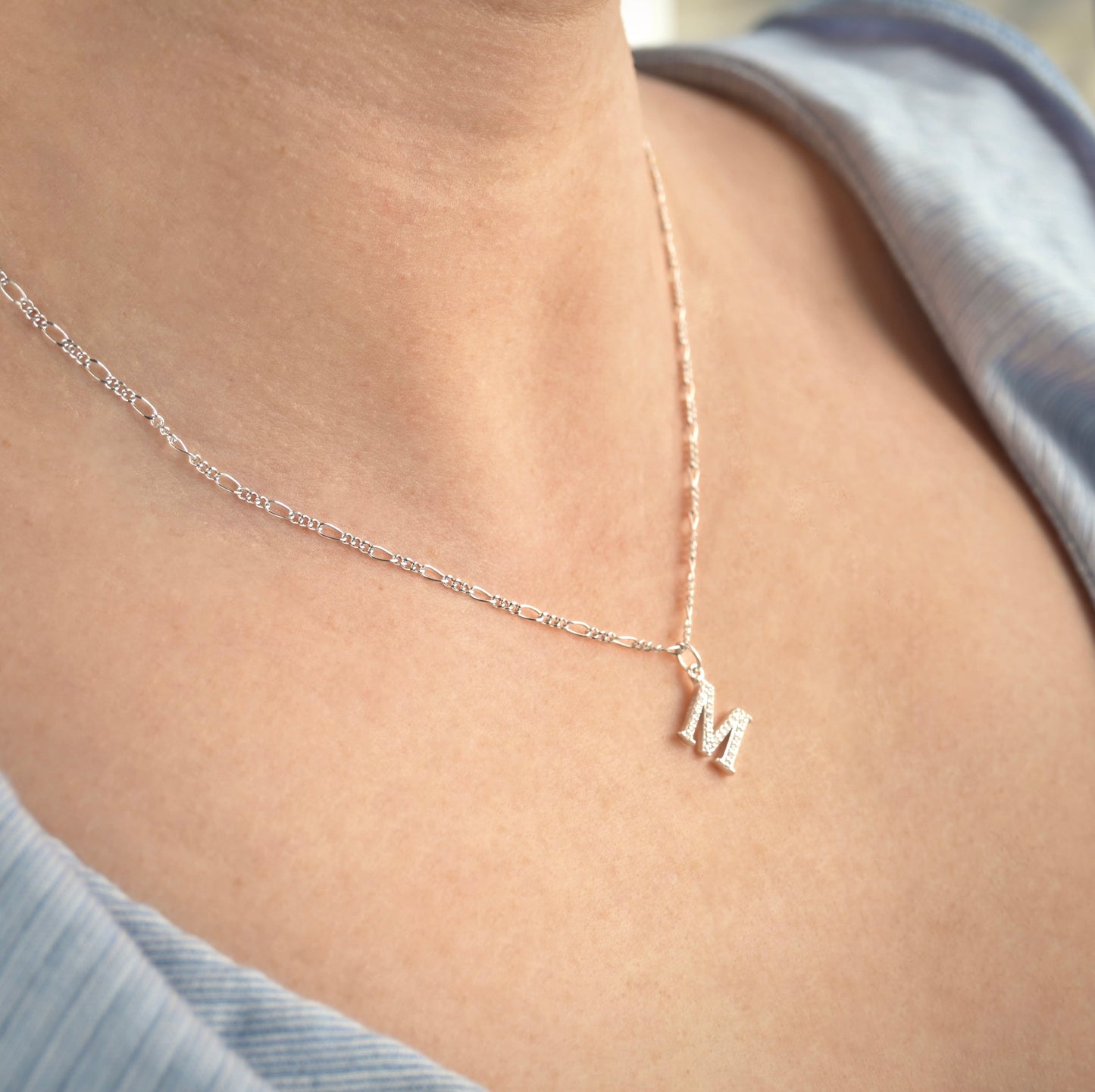 Silver CZ initial necklace with a figaro chain on a person's neck