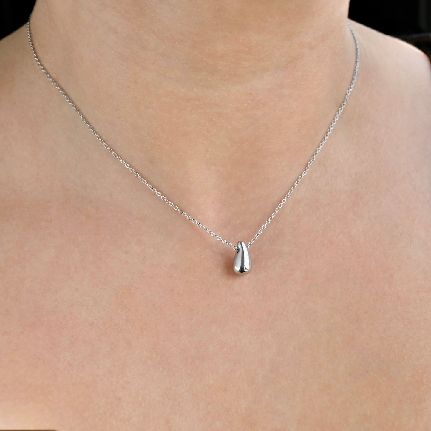 Silver  waterdrop necklace with a pendant on a person's neck against a neutral background