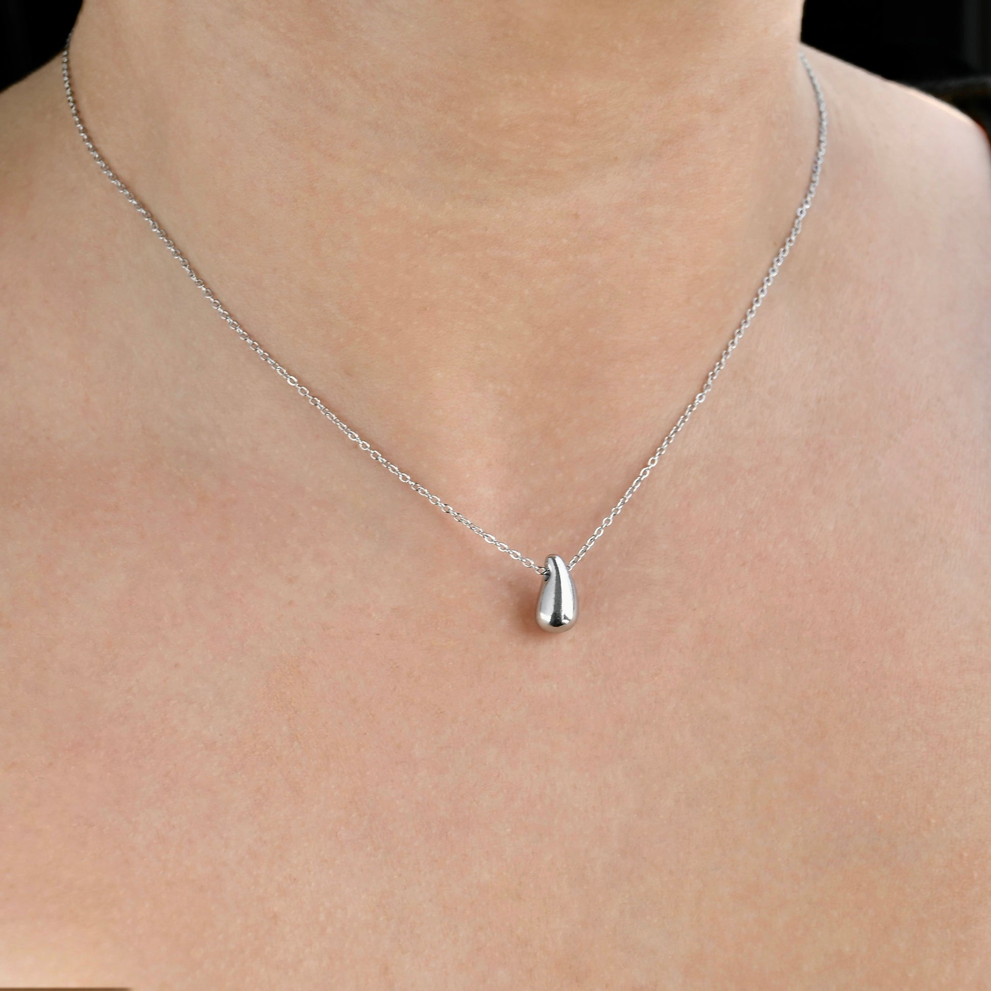 Silver  waterdrop necklace with a pendant on a person's neck against a neutral background