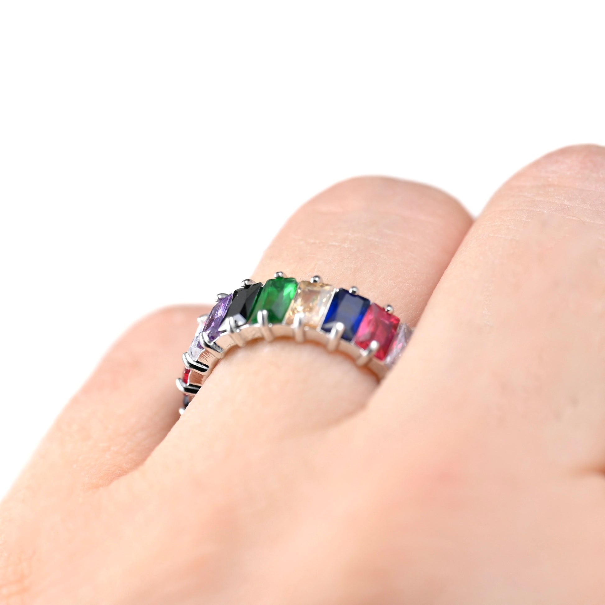 Silver ring with rainow stones on a finger against a white background