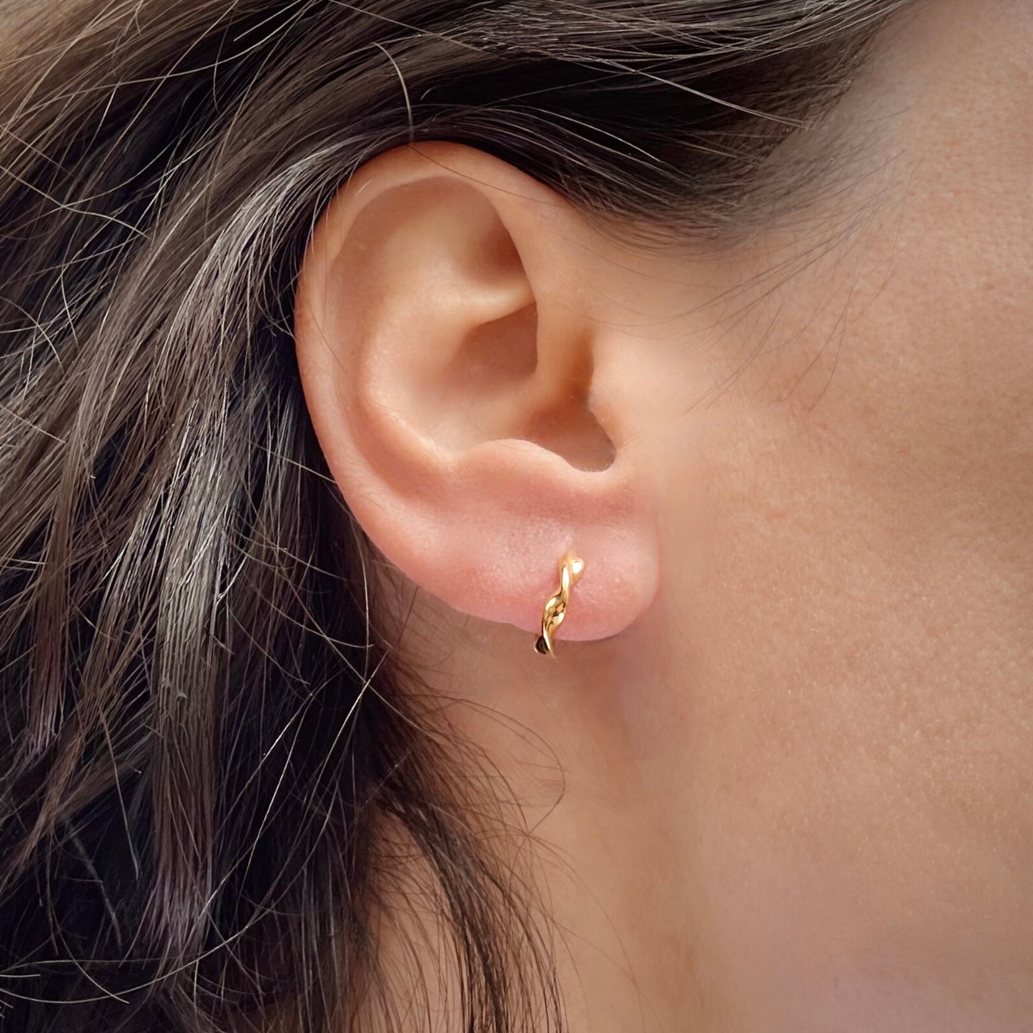 Close-up of an ear wearing a gold hoop earring with hair partially covering the frame.