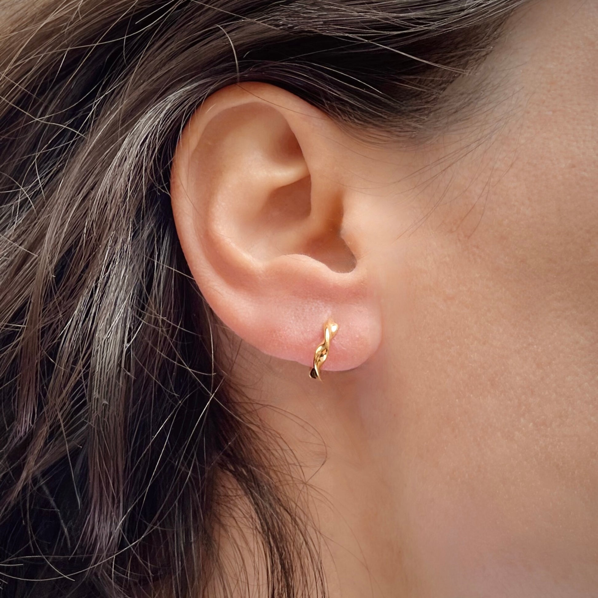 Close-up of an ear wearing a gold hoop earring with hair partially covering the frame.