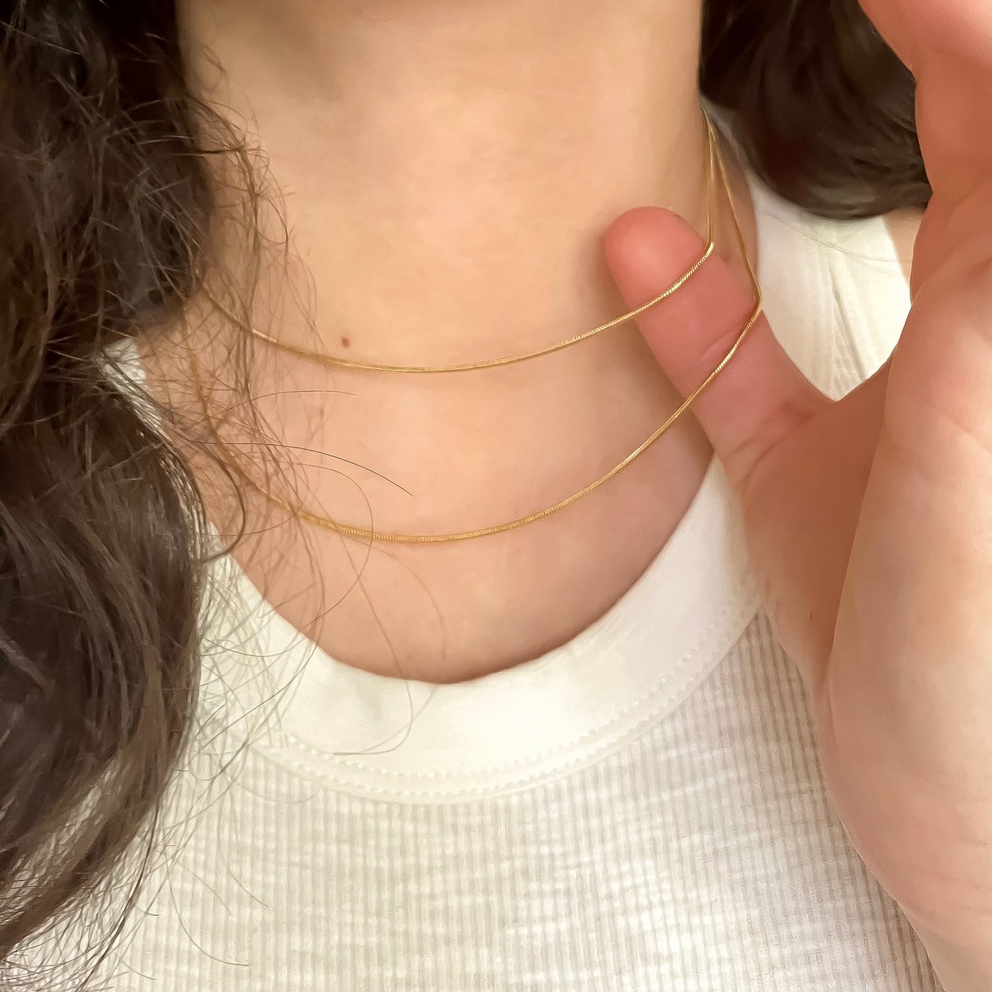 Close-up front view of a person wearing a delicate gold necklace set with thin snake chains 
