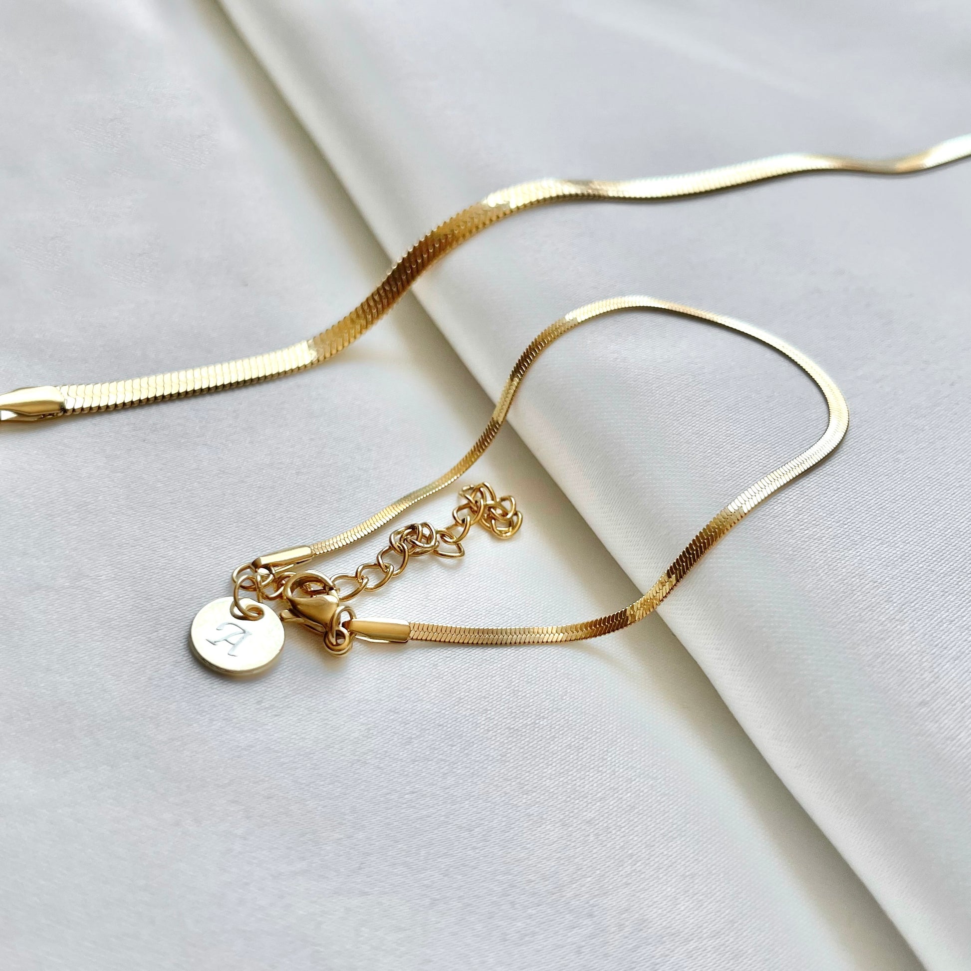 Gold bracelet with a small round initial charm on a light gray background