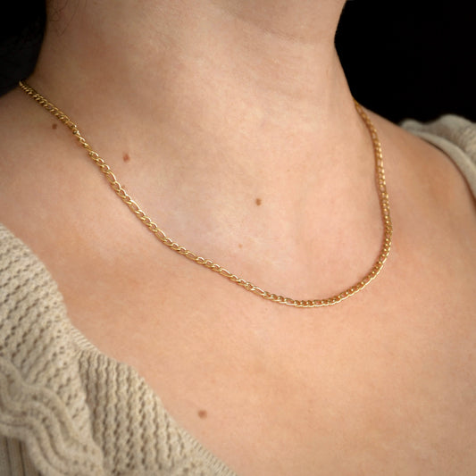 Dainty Gold chain necklace on a person wearing a beige sweater against a black background