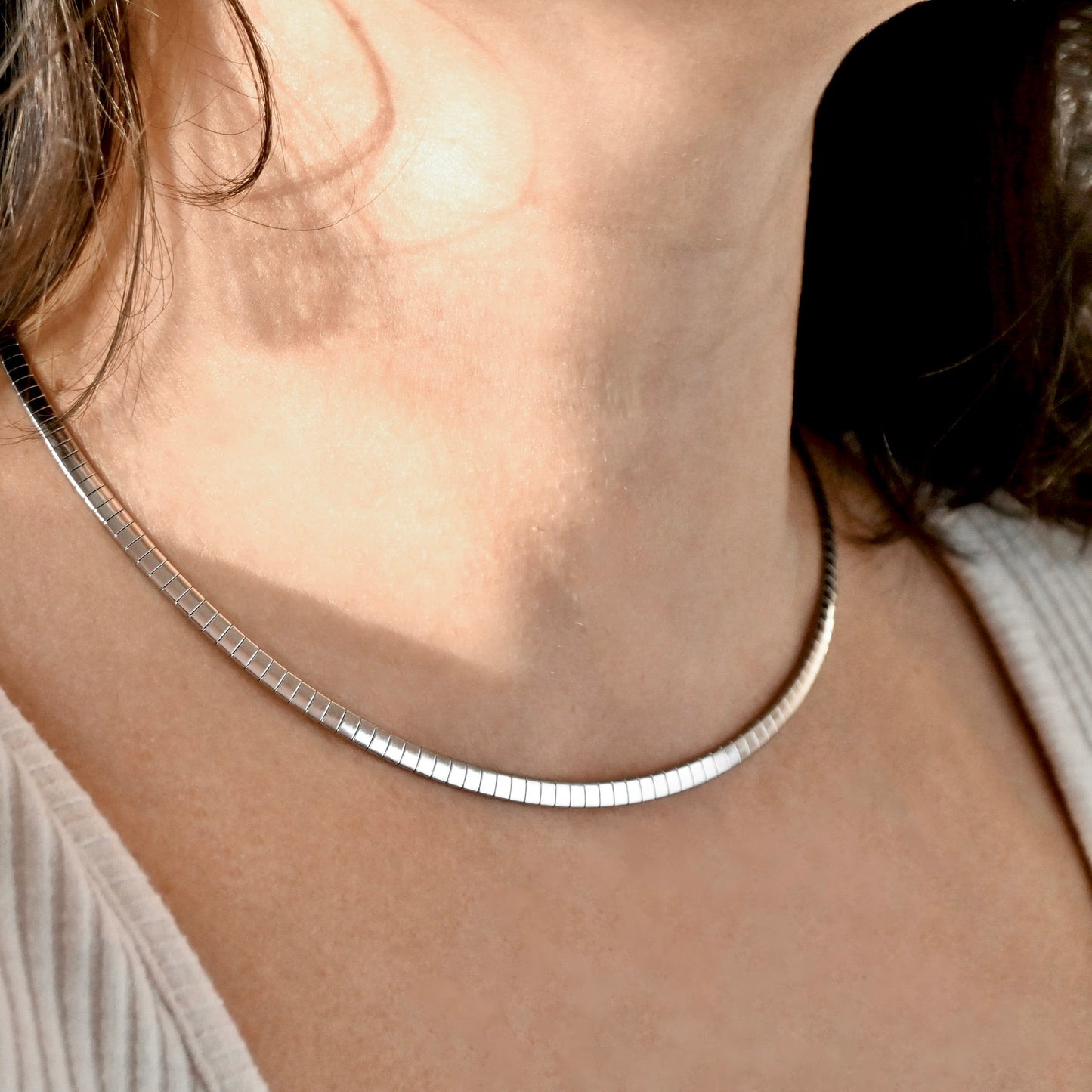 A close-up of a person's neck and upper chest wearing a thin silver snake chain necklace.