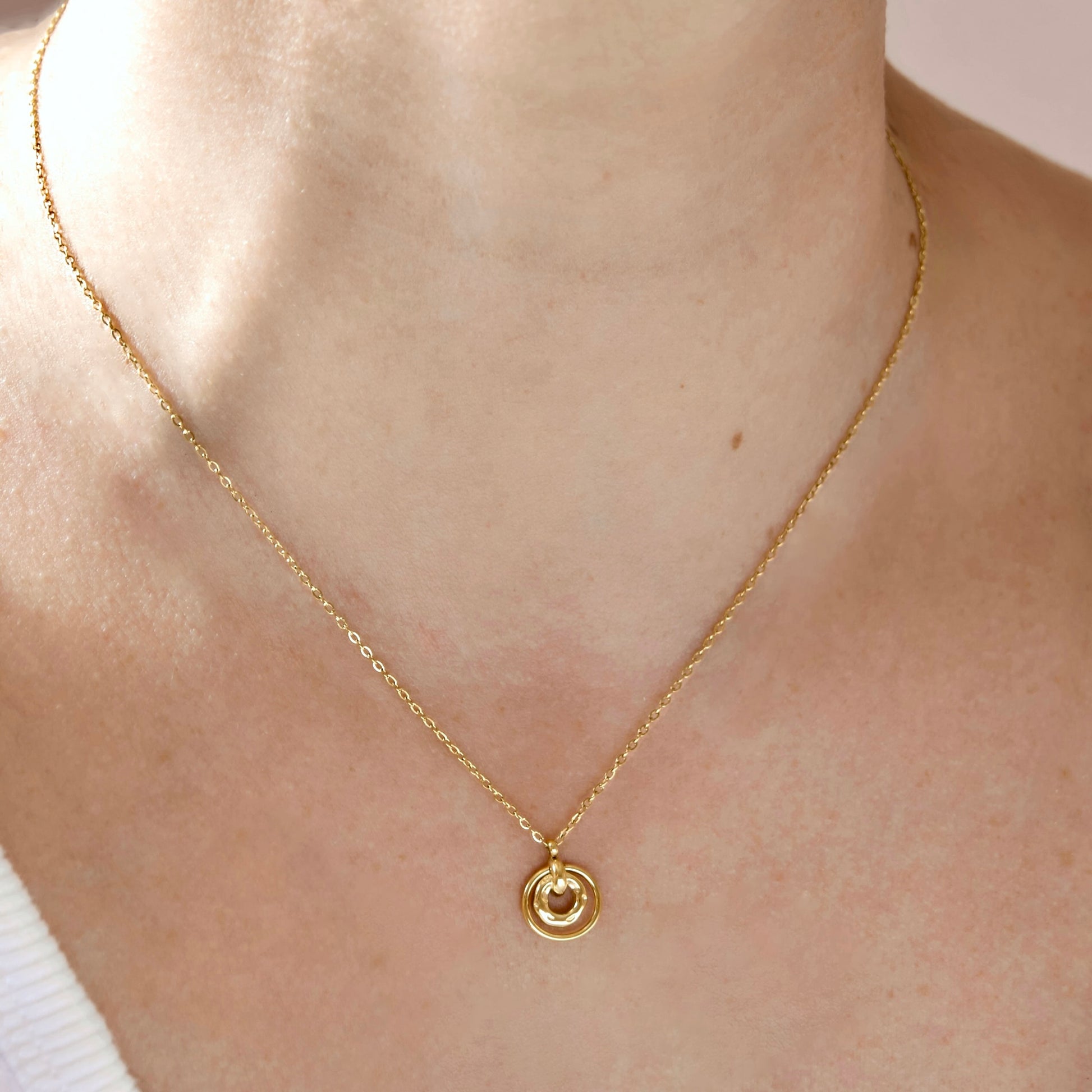 A delicate gold chain necklace with a small concentric circle pendant, shown worn on a person's neck.