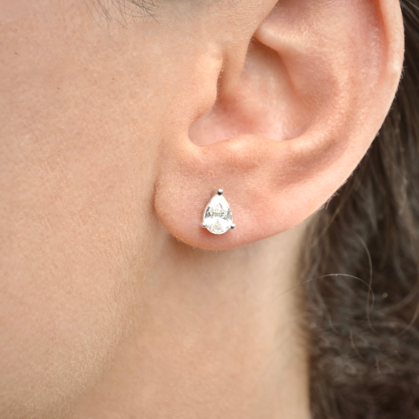 Close-up of an ear wearing a silver pear-shaped stud earring.