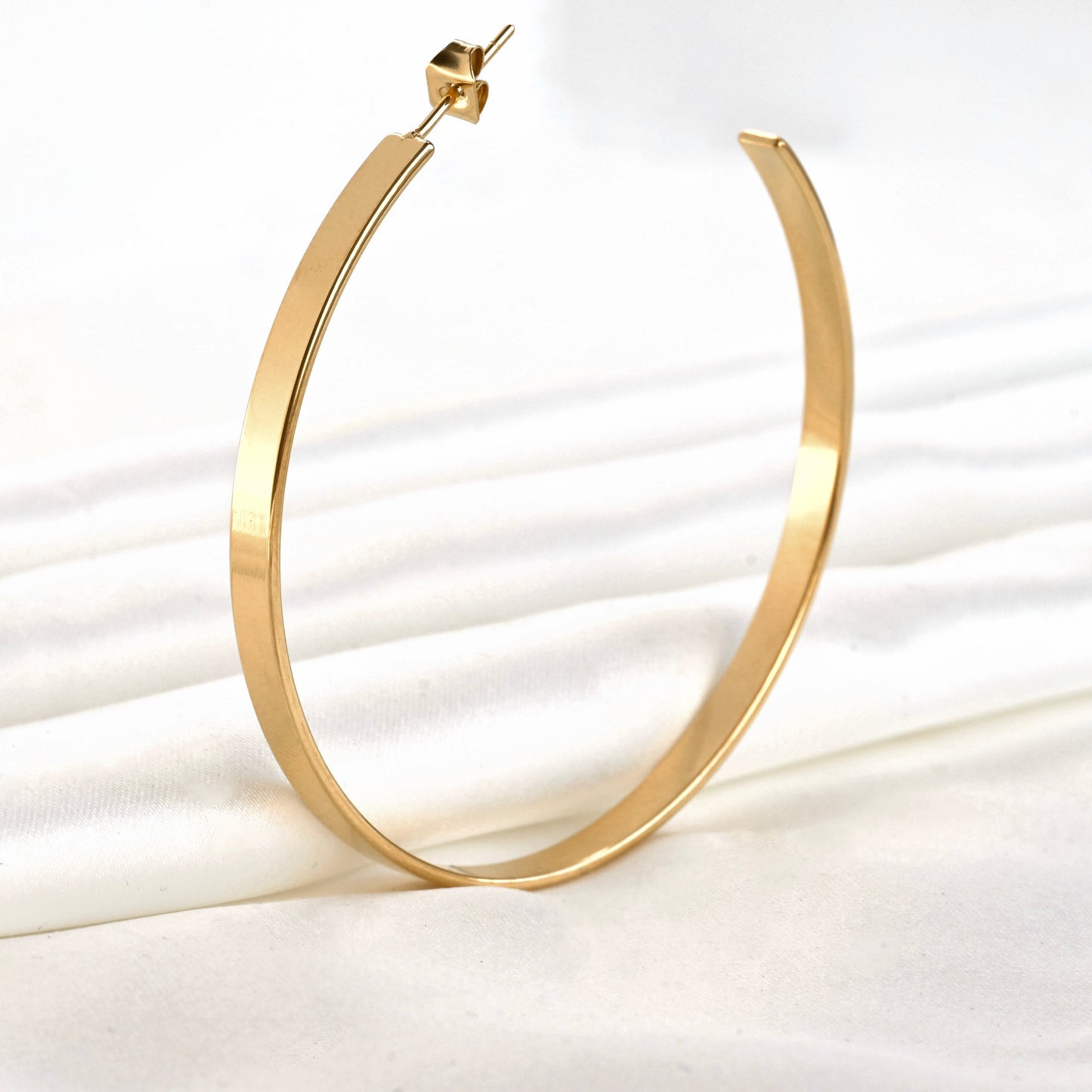 Gold hoop earring on a white fabric background