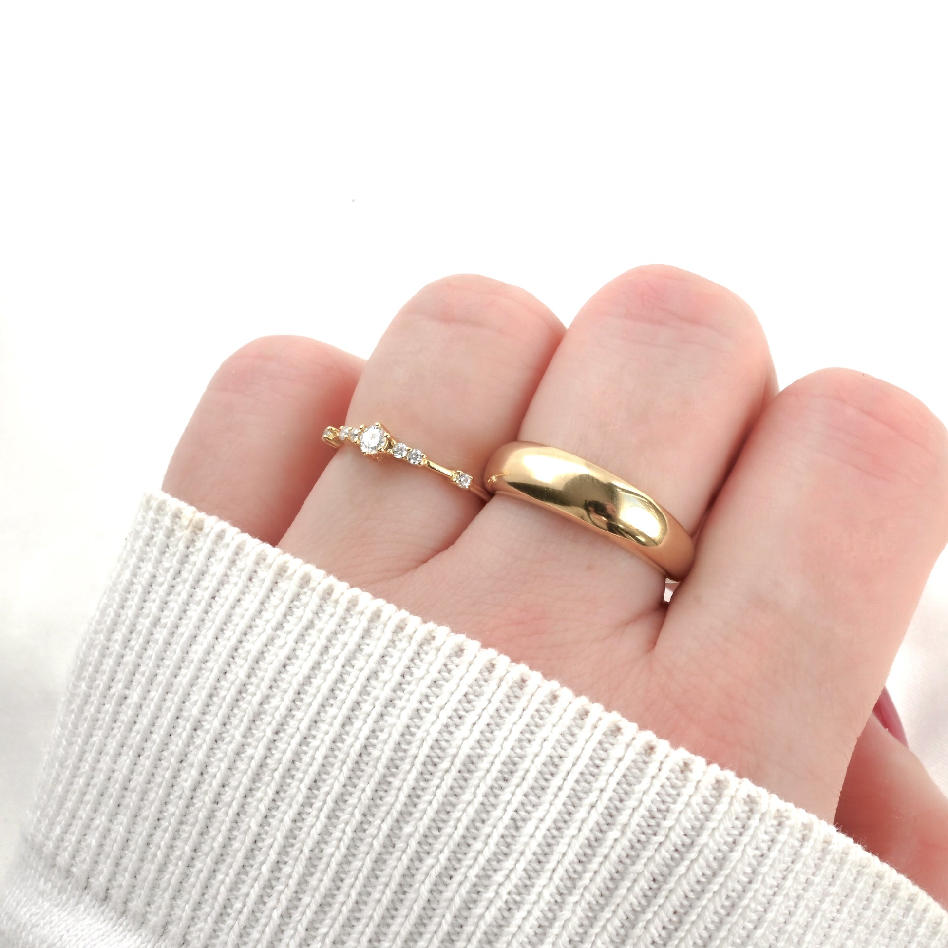 Gold ring with a diamond stacked with chunky dome ring on a finger against a white background