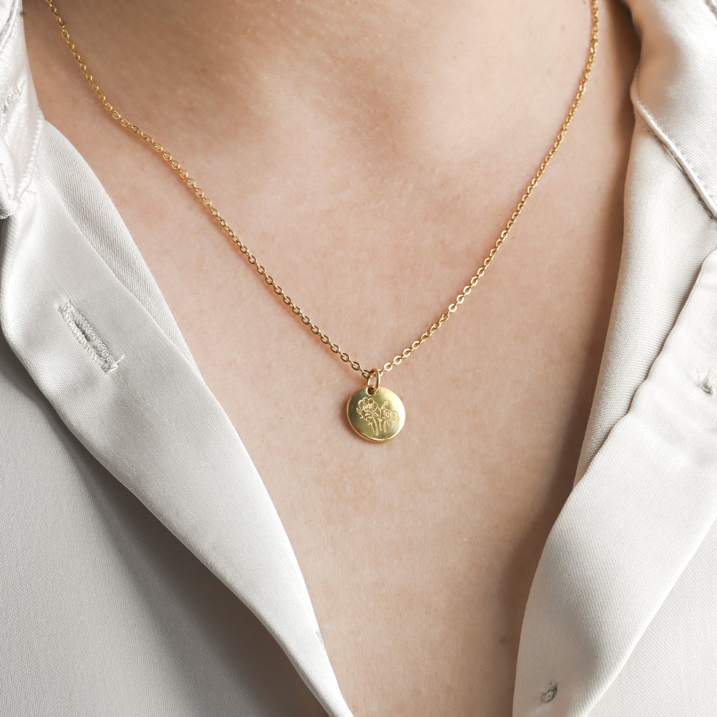 Gold necklace with a 12mm round pendant with flower engraving on a person wearing a white shirt.