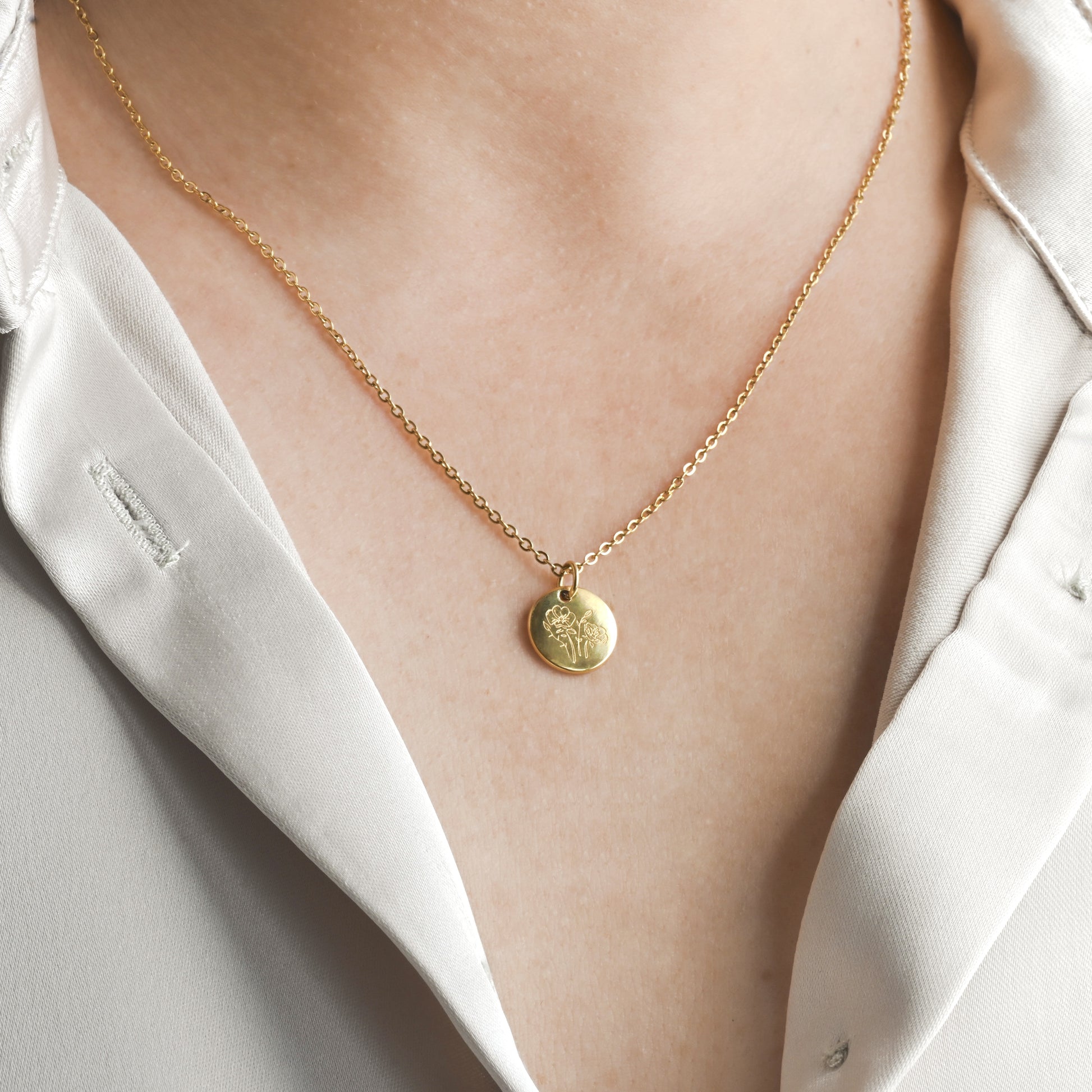 Gold necklace with a 12mm round pendant with flower engraving on a person wearing a white shirt.