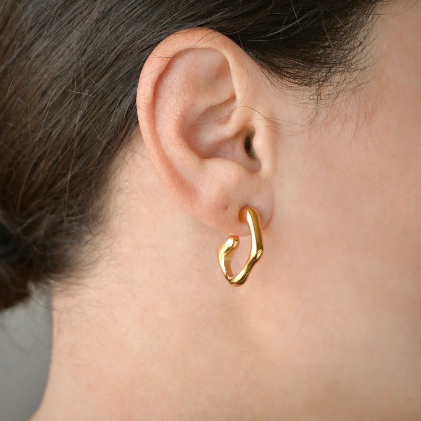 Close-up of gold hoop earring worn by a person with a neutral background