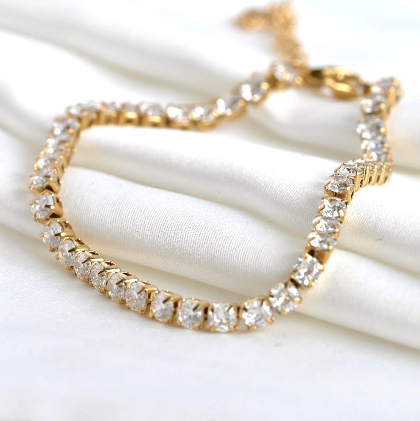 Close up of gold bracelet with clear CZ on a white fabric background
