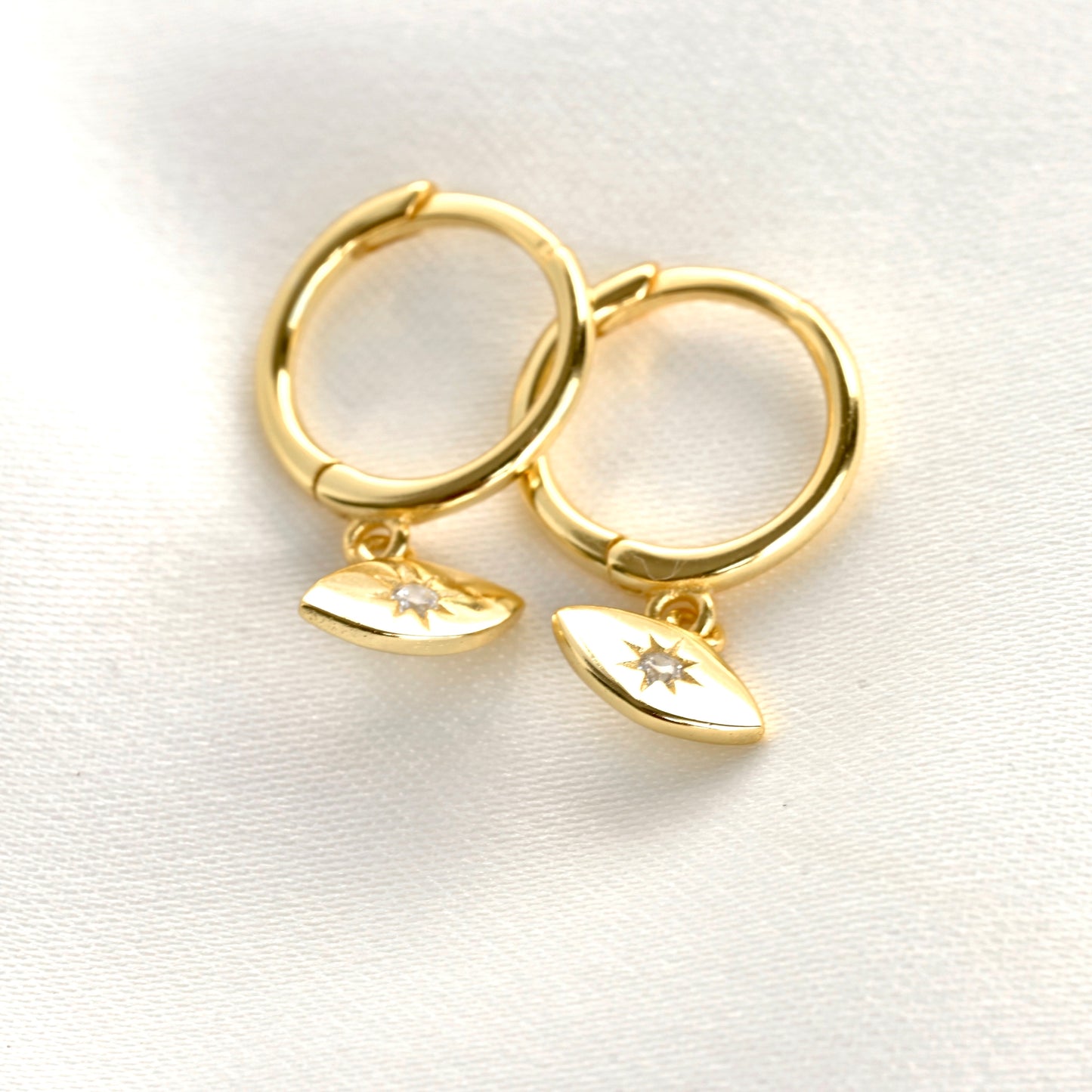 Gold hoop earrings with evil eye charms on a white background