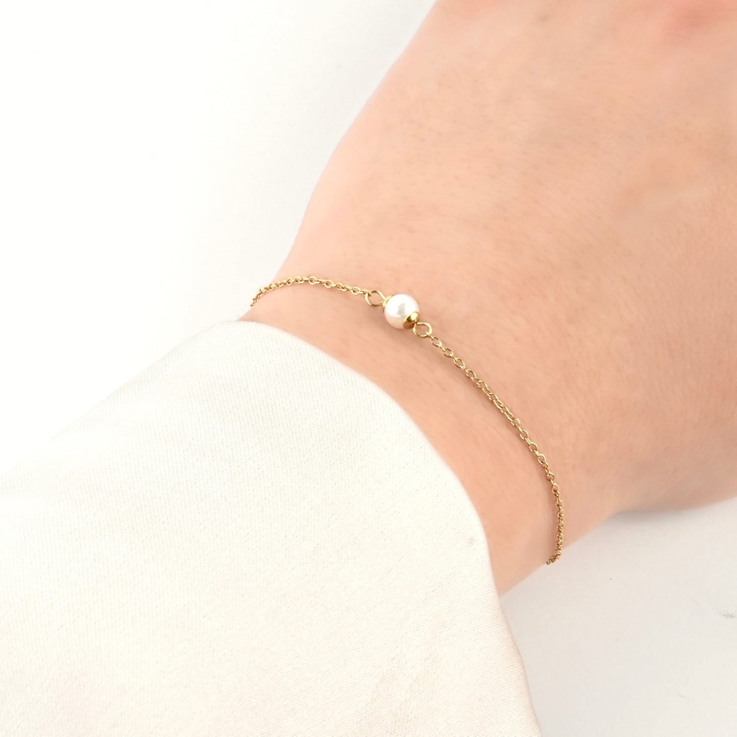 Gold single pearl bracelet  on a wrist against a white background