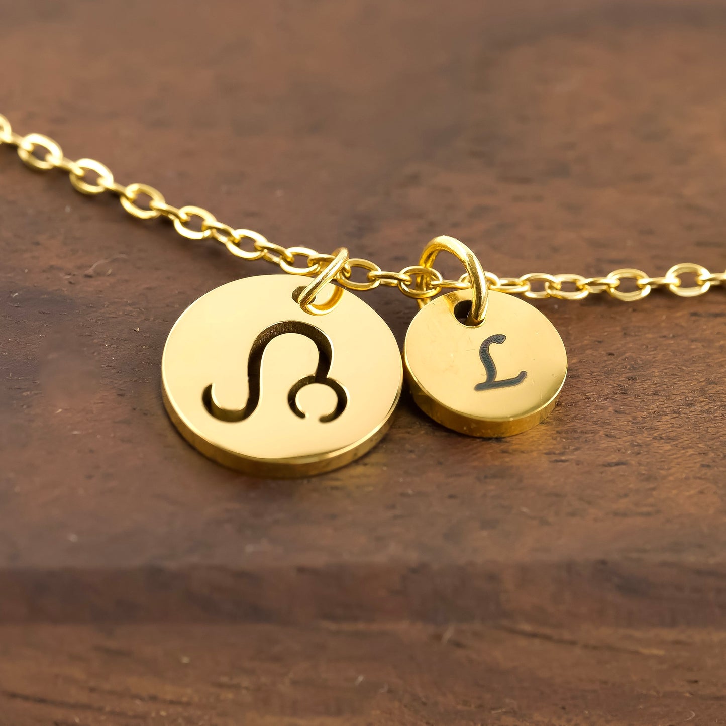 Gold necklace with zodiac symbol and letter 'L' on a wooden surface