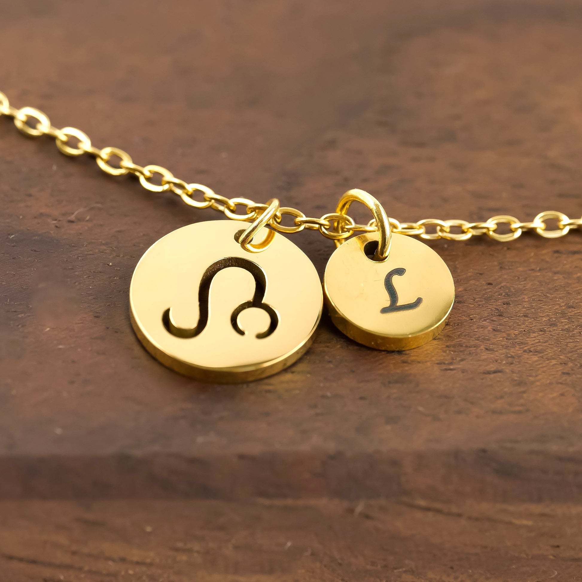 Gold necklace with zodiac symbol and letter 'L' on a wooden surface