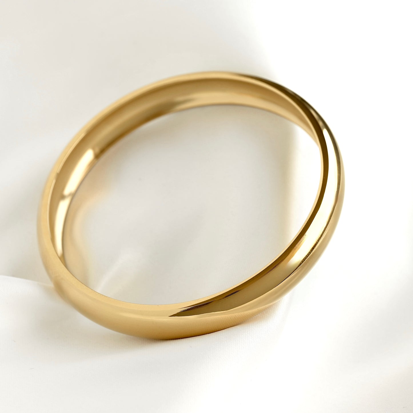 A polished slim gold band bracelet photographed on a clean white background.