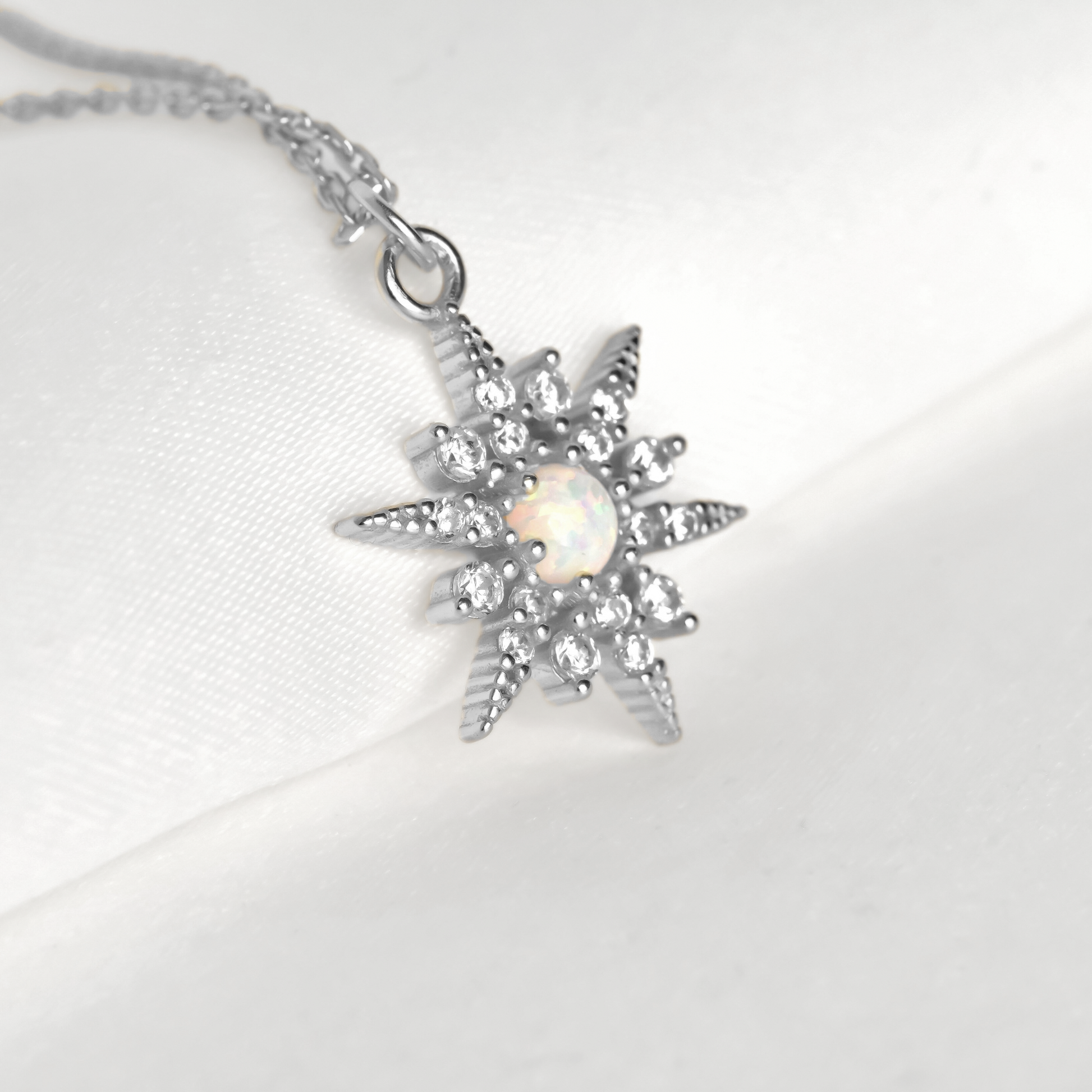 Silver starburst pendant with a central opal stone and smaller clear gemstones around on a white background