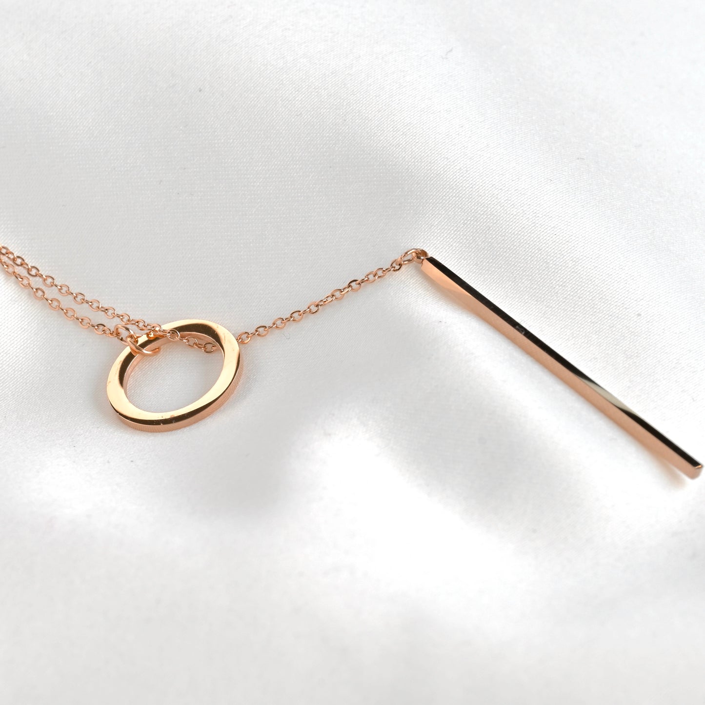Rose gold necklace with a circular pendant and a straight bar threaded in the circle on a white background
