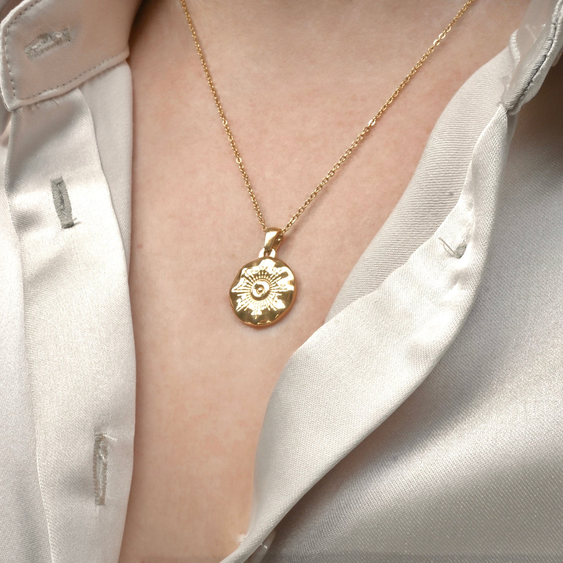 Sun medallion necklace worn by a person in a white shirt.