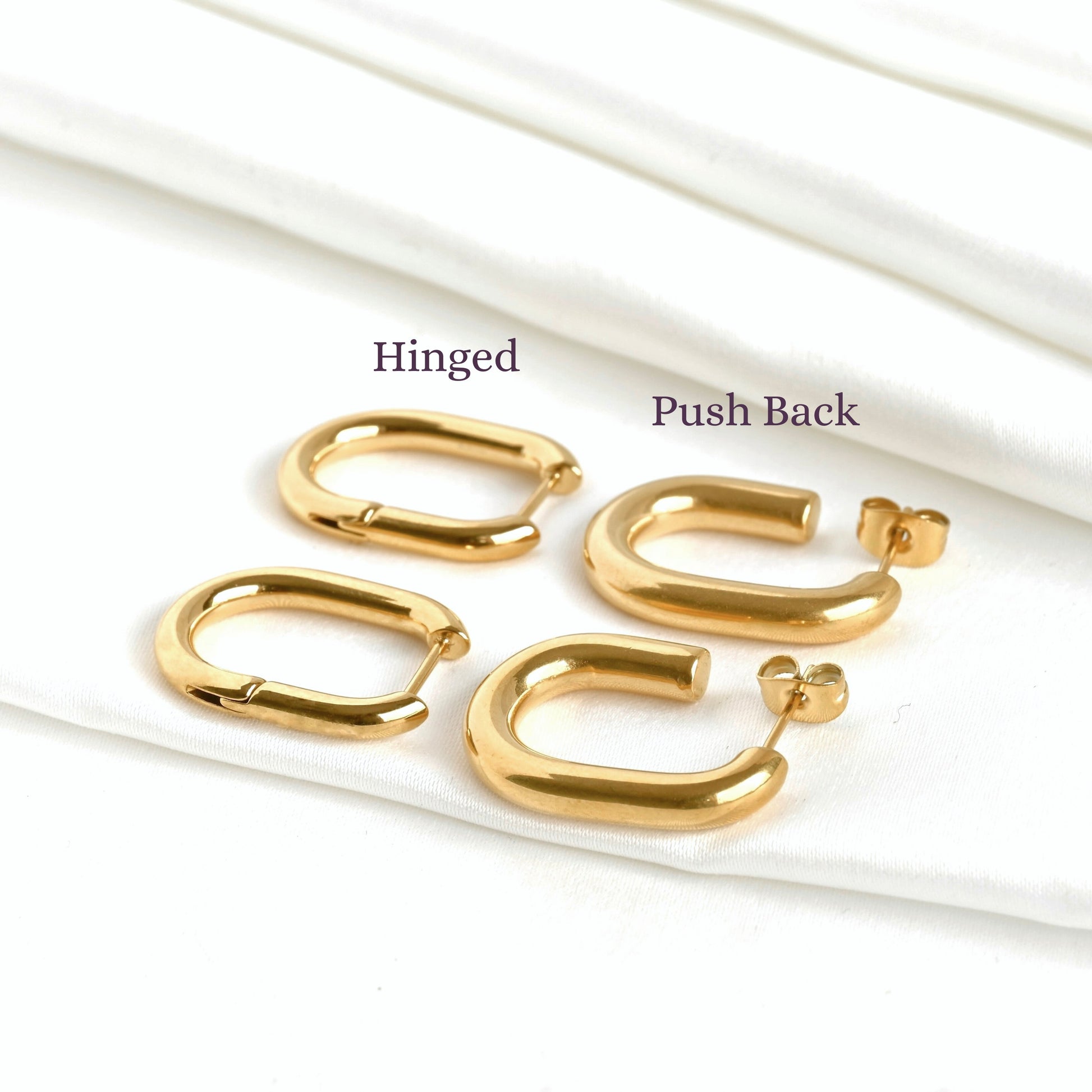 Gold oblong hoop earrings flat on a white satin fabric  with 'Hinged' and 'Push Back' labels 