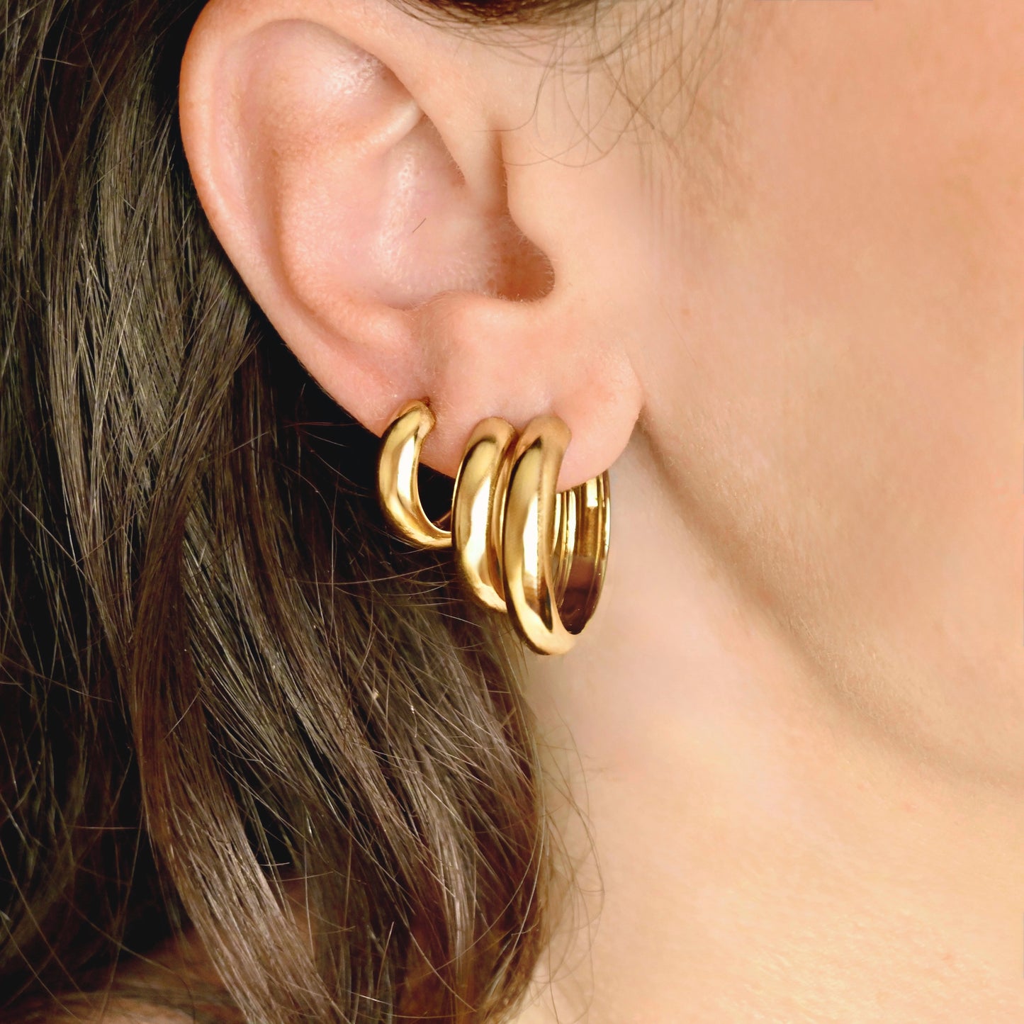A close-up of a person's ear wearing a set of three polished gold hoop earrings.
