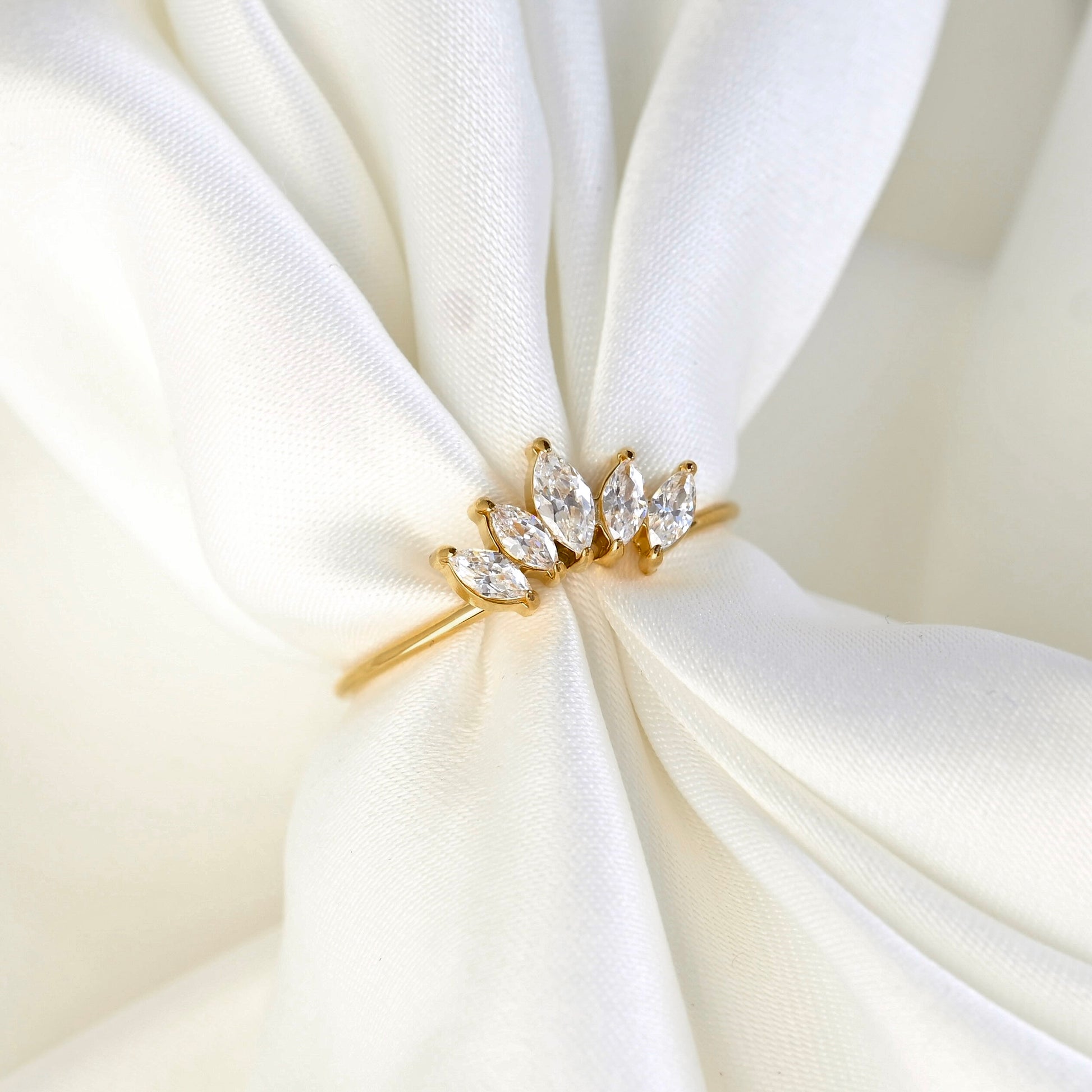 Gold ring with marquise-shaped diamonds on a white fabric background