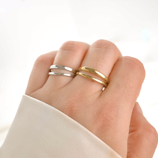 Hand wearing two double row rings, one gold and one silver, on a light background