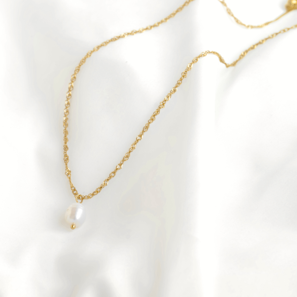 A delicate gold chain necklace featuring a single white freshwater pearl pendant, displayed on a soft white fabric background.
